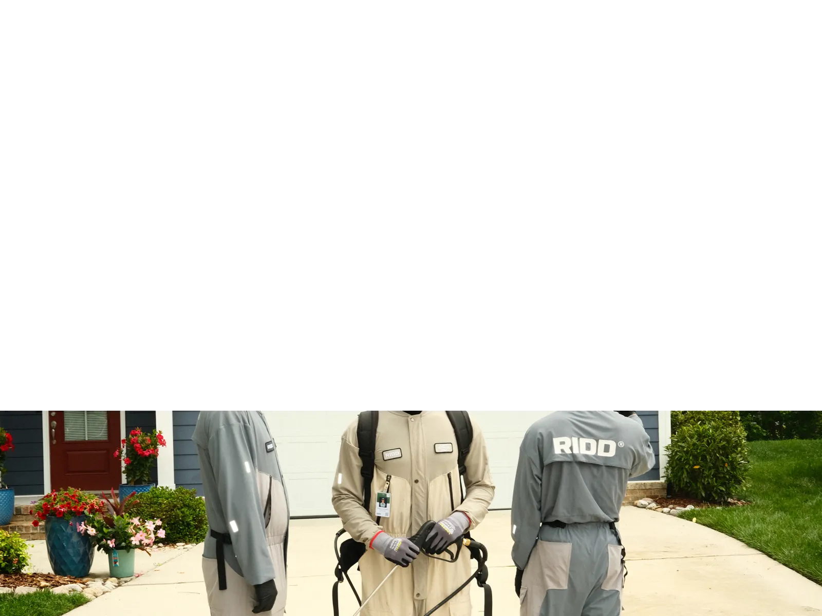 Three pest control workers wearing protective suits and gear standing on a suburban driveway preparing for treatment.