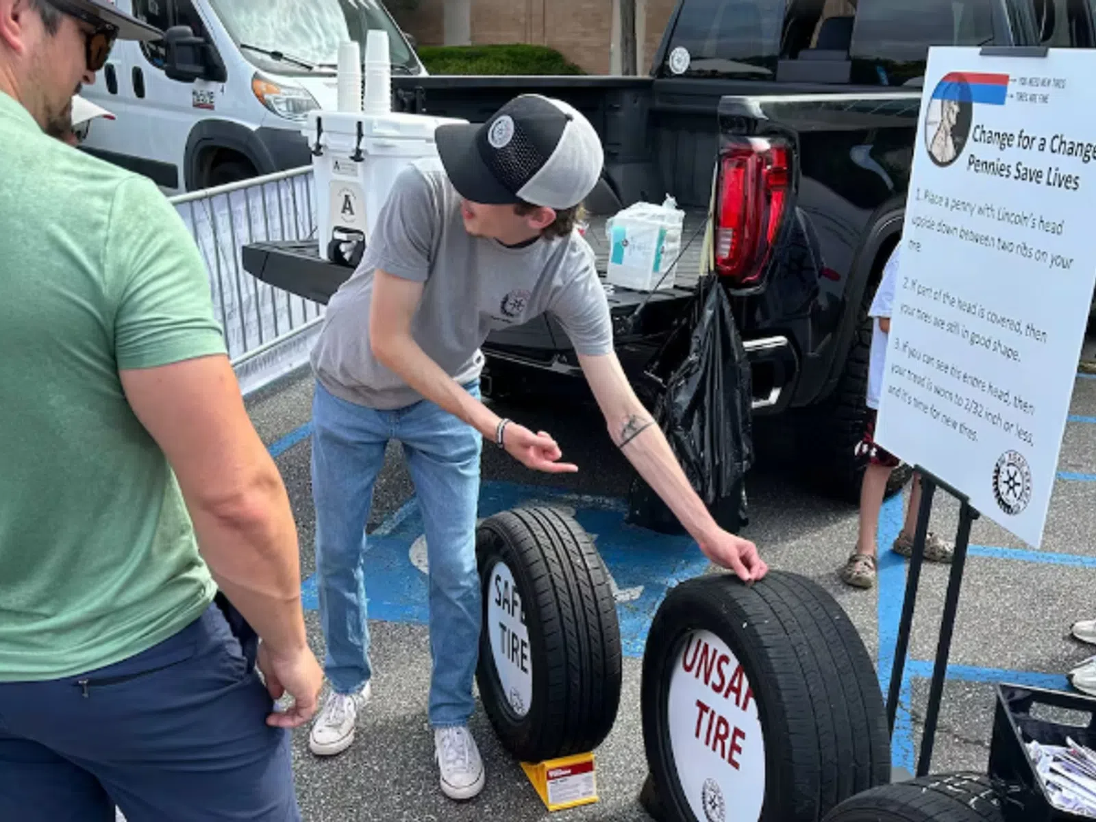 Man explains safe versus unsafe tire conditions using tires as visual aids at outdoor event.