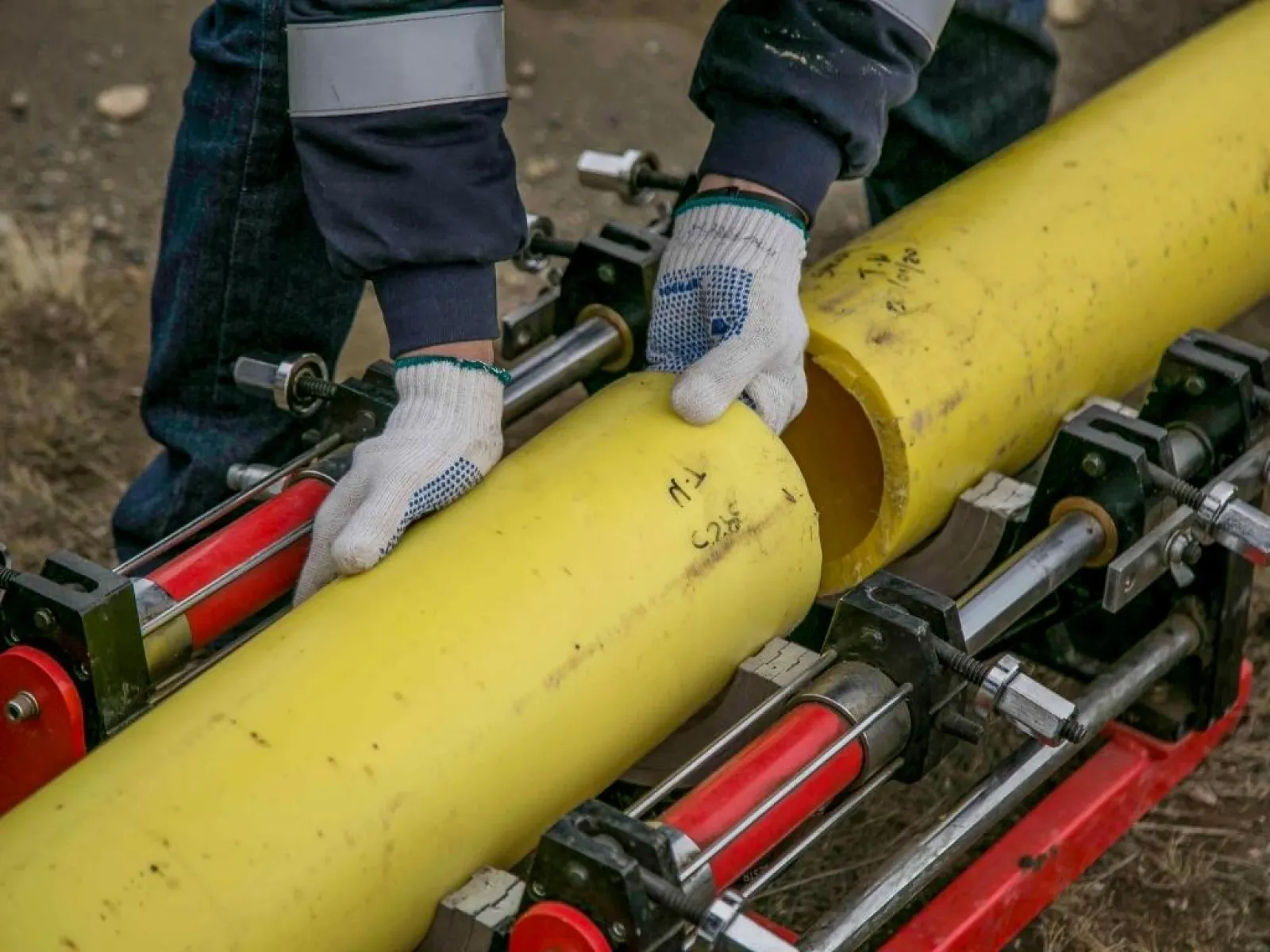 Workers wearing gloves aligning yellow plastic pipes for welding on a machine outdoors