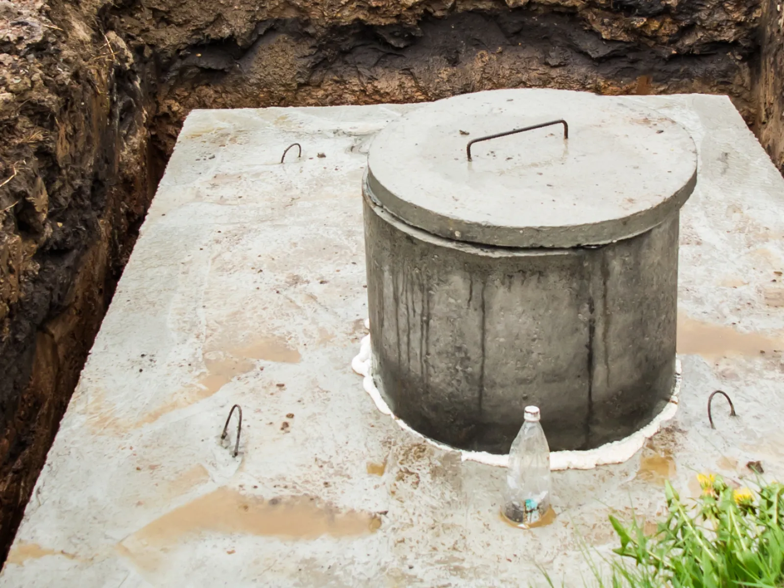 A concrete water cistern installed in a freshly dug ground surrounded by soil and grass.