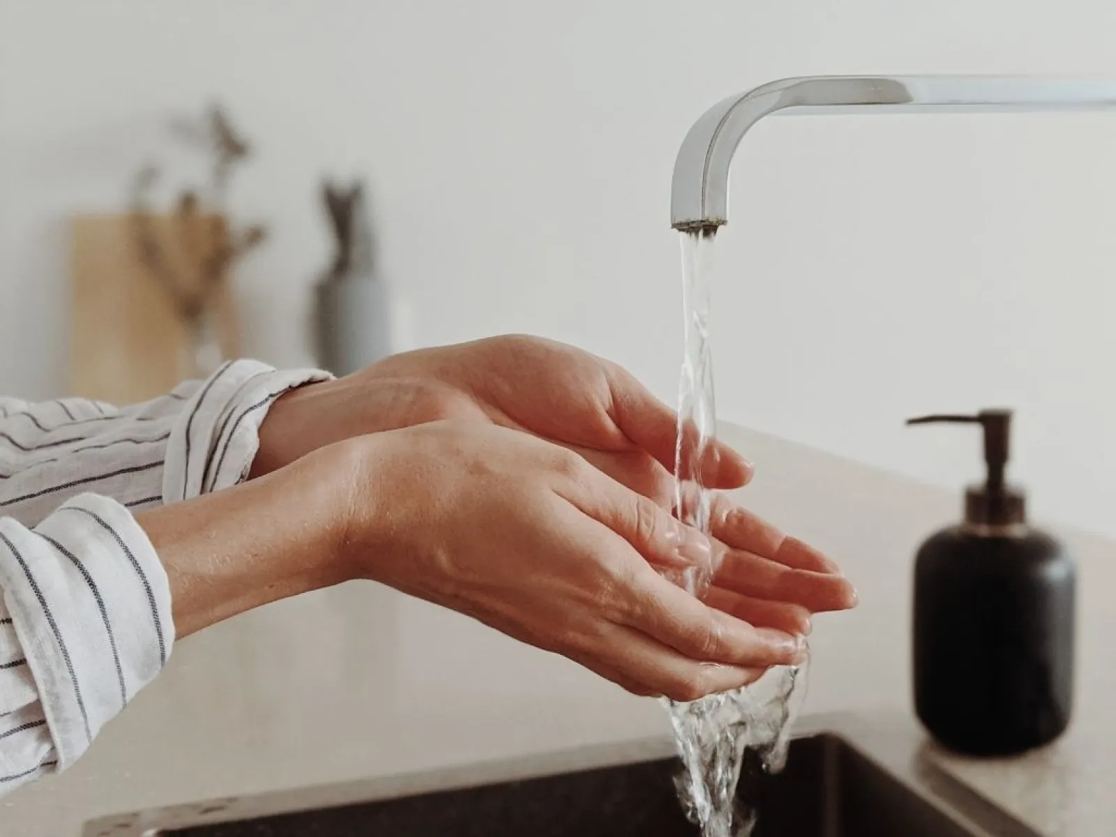 Person washing hands under running water from a modern faucet in a clean kitchen sink area.