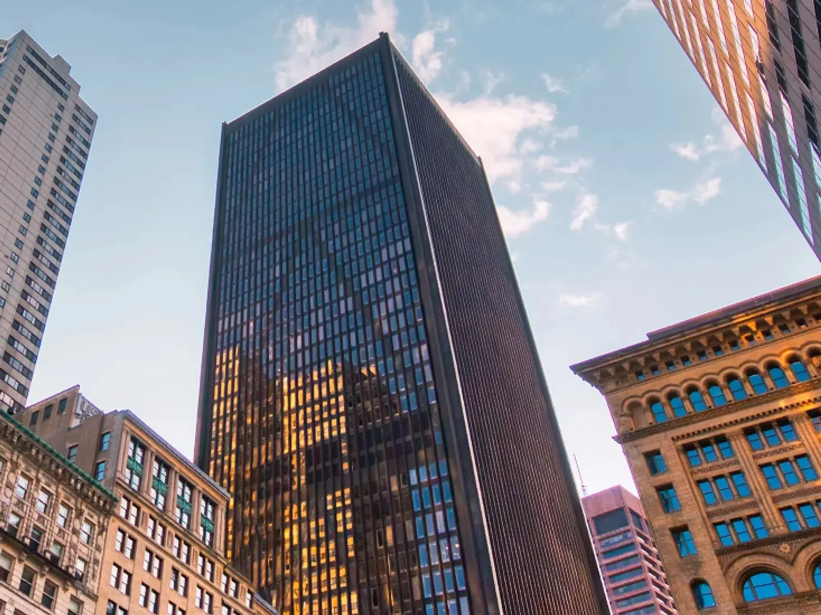 Low angle view of modern and historic skyscrapers under a partly cloudy sky at sunset.