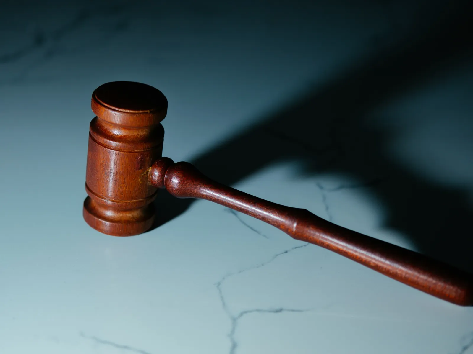 Wooden judge's gavel casting a shadow on a marble surface in dramatic lighting.
