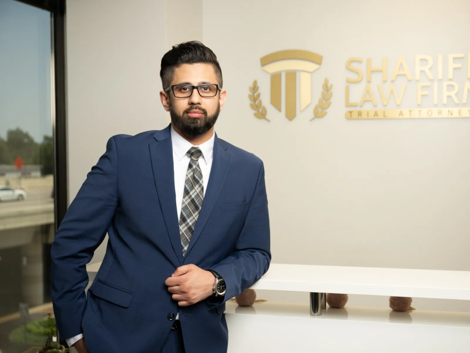 Professional man in blue suit standing in office lobby of Shariff Law Firm with logo on wall.