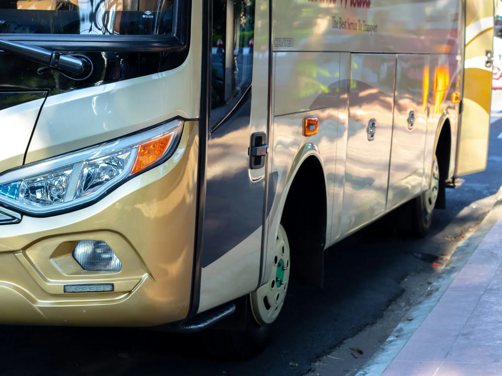 Close-up of a cream and gold modern tour bus front side parked on a city street under bright sunlight