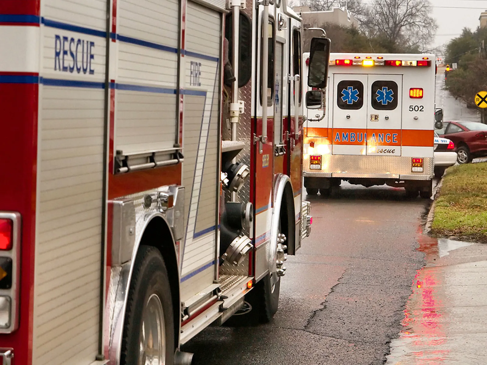 Fire truck and ambulance parked on a wet street during an emergency response in a residential area.