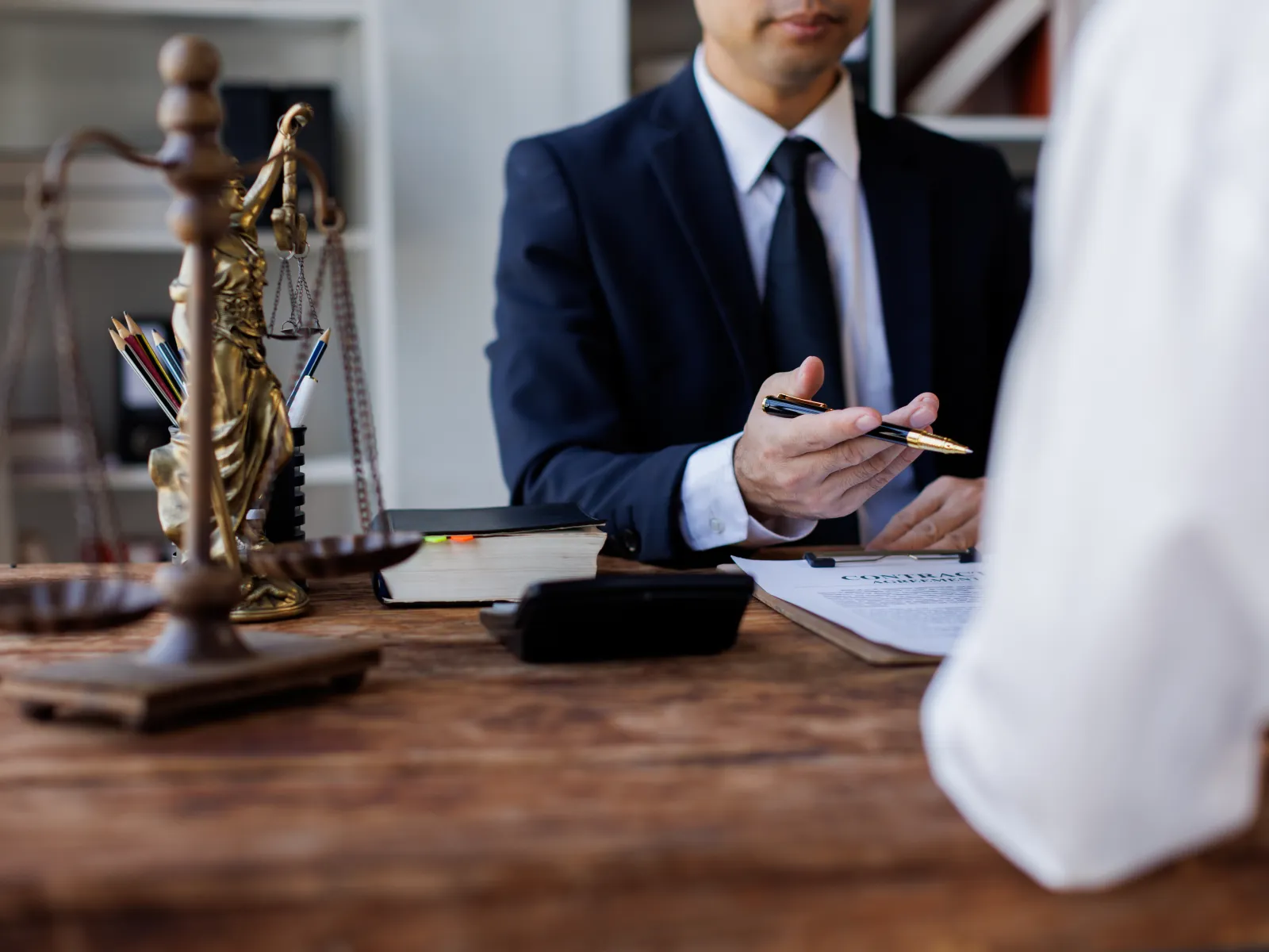 Lawyer in suit discussing legal documents with client, with scales of justice on wooden desk in office.