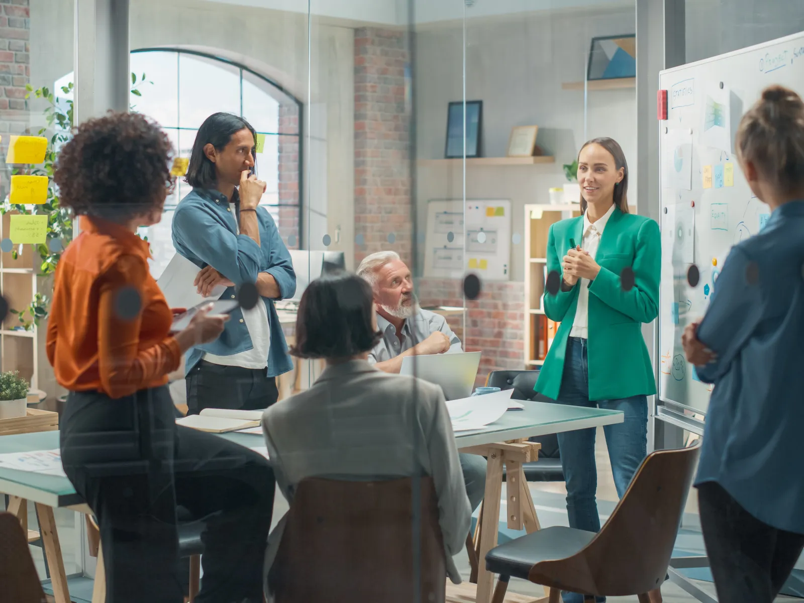 Team of diverse colleagues brainstorming and discussing ideas in modern office meeting with whiteboard and sticky notes.