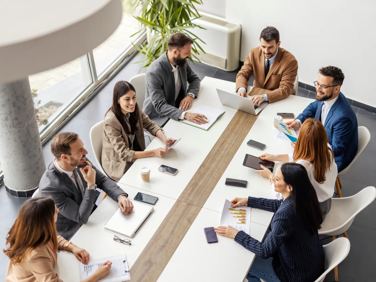 Team of six people working together on laptops and documents in a bright modern office with brick walls.