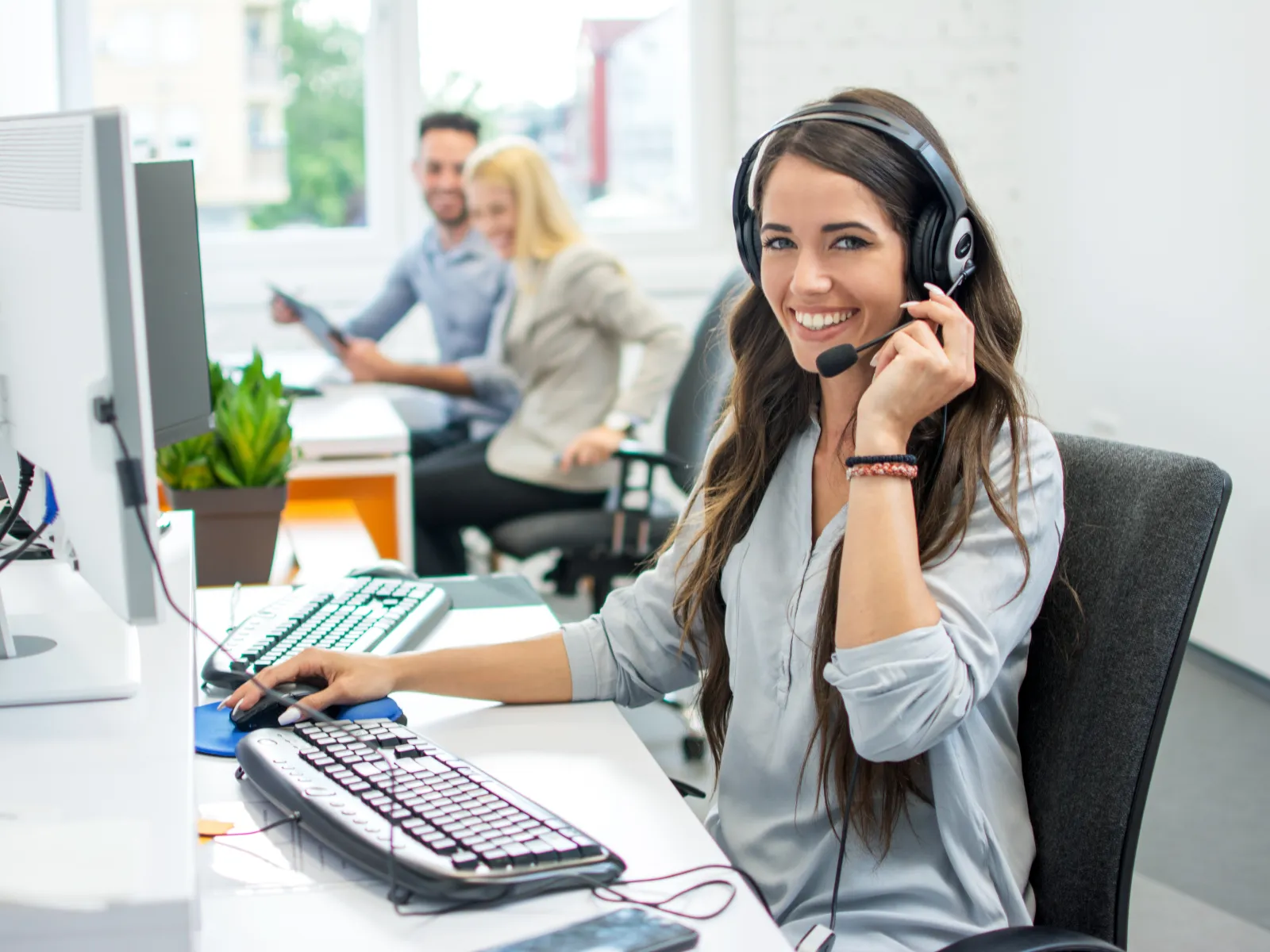 Smiling customer service representative wearing headset working on computer in modern office setting.