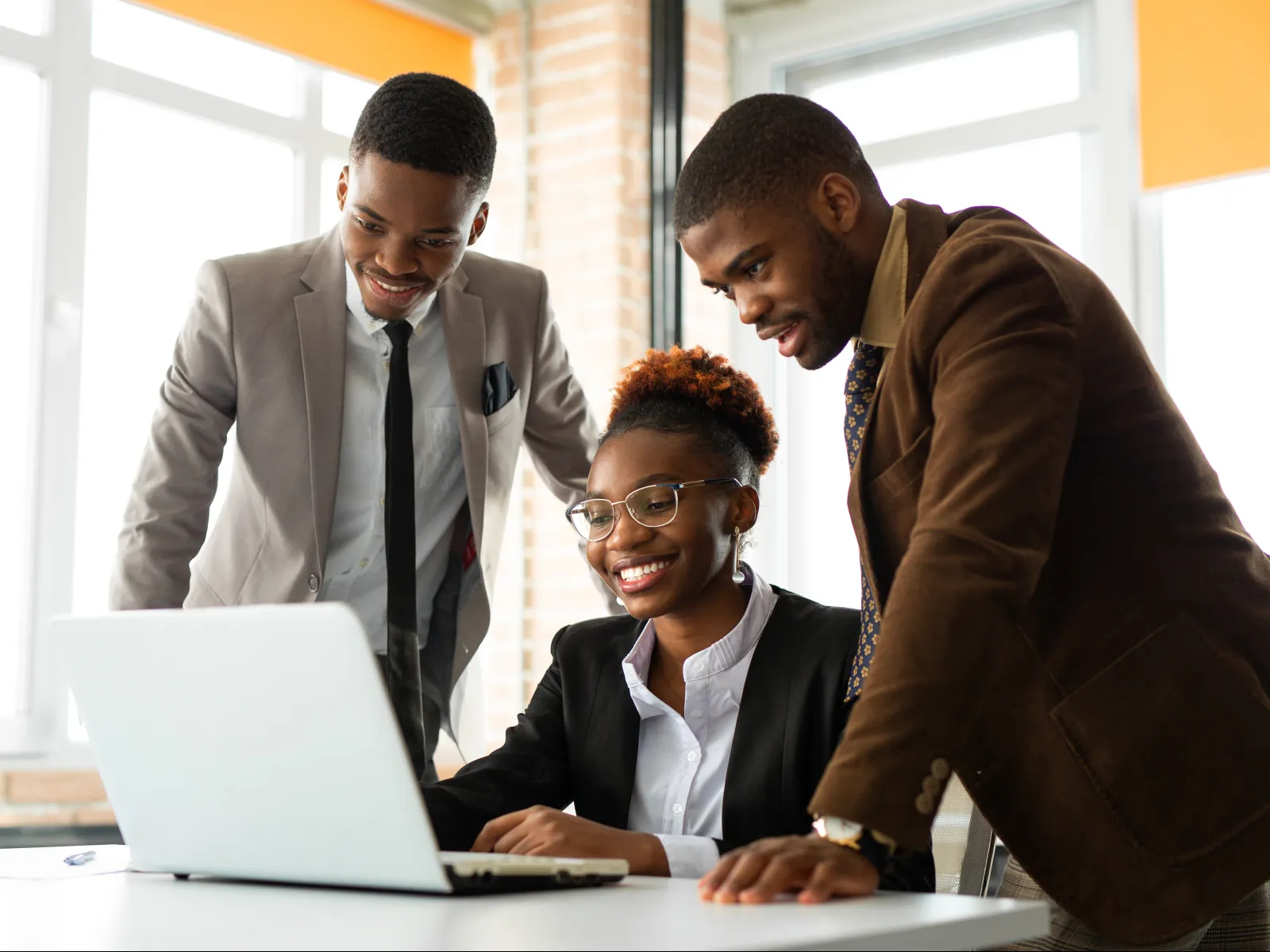 Three young professionals collaborating and smiling while working on a laptop in a bright office.