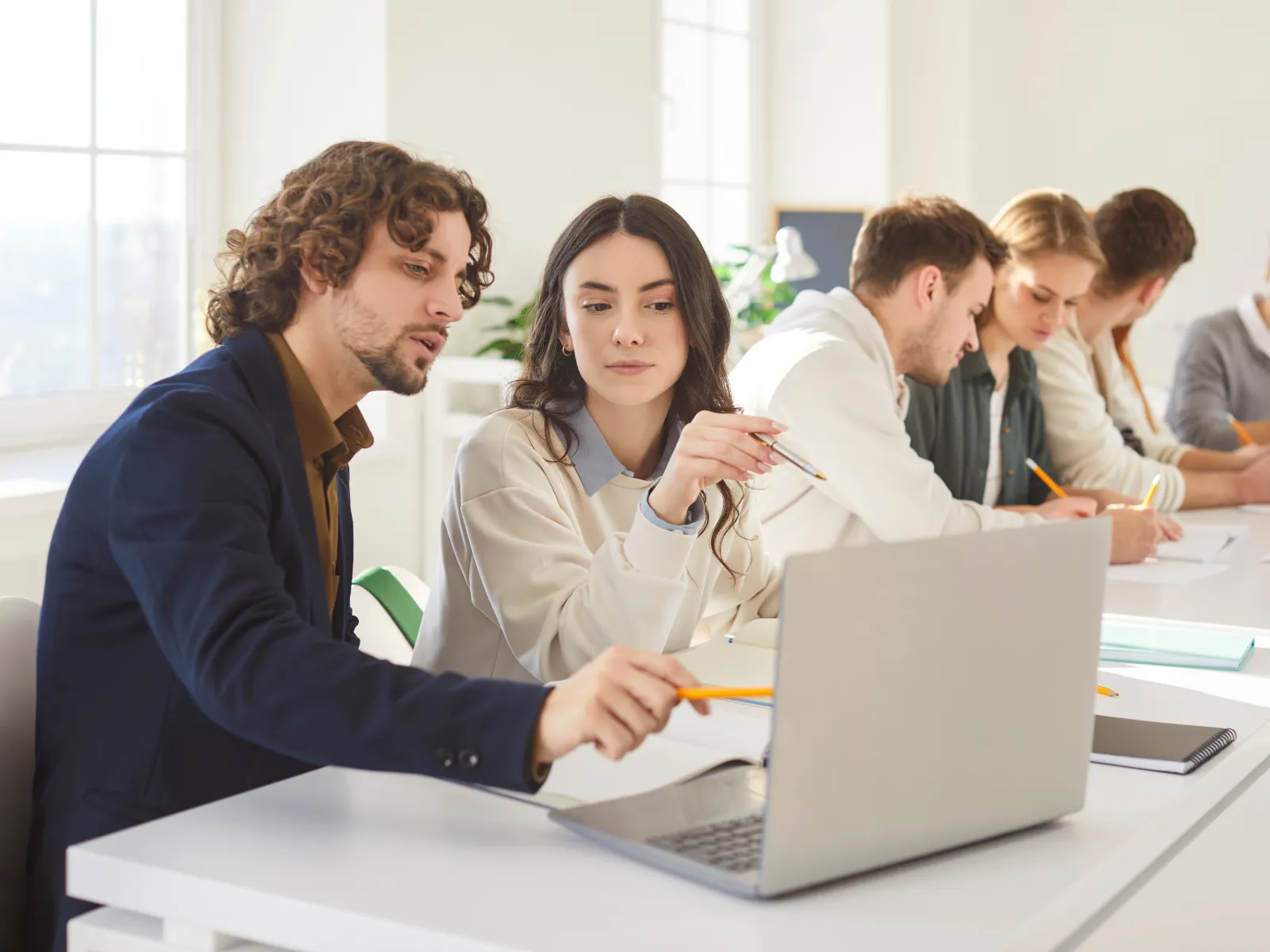 Group of young professionals collaborating in a bright modern office all focused on laptops and notes.