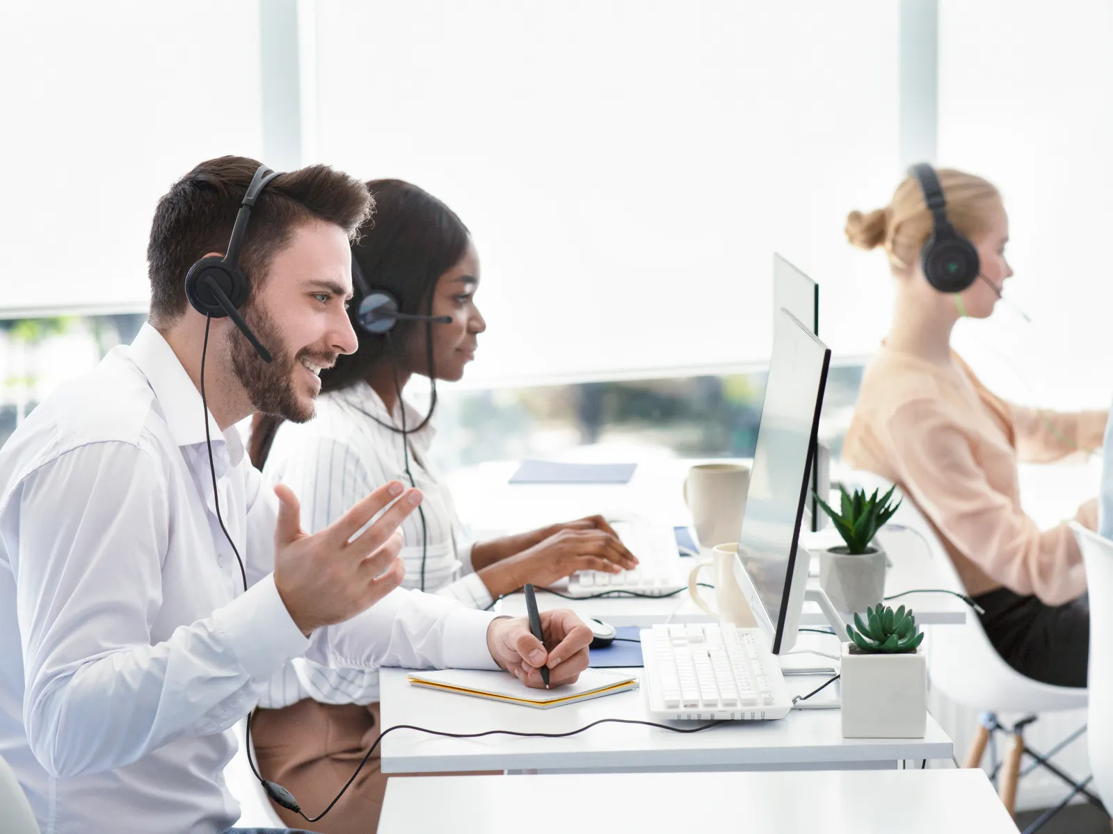 Customer service team wearing headsets working at computers in a bright modern office environment.