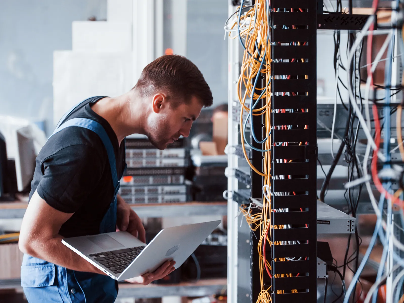 Technician working with laptop on server rack maintenance in a data center filled with network cables.