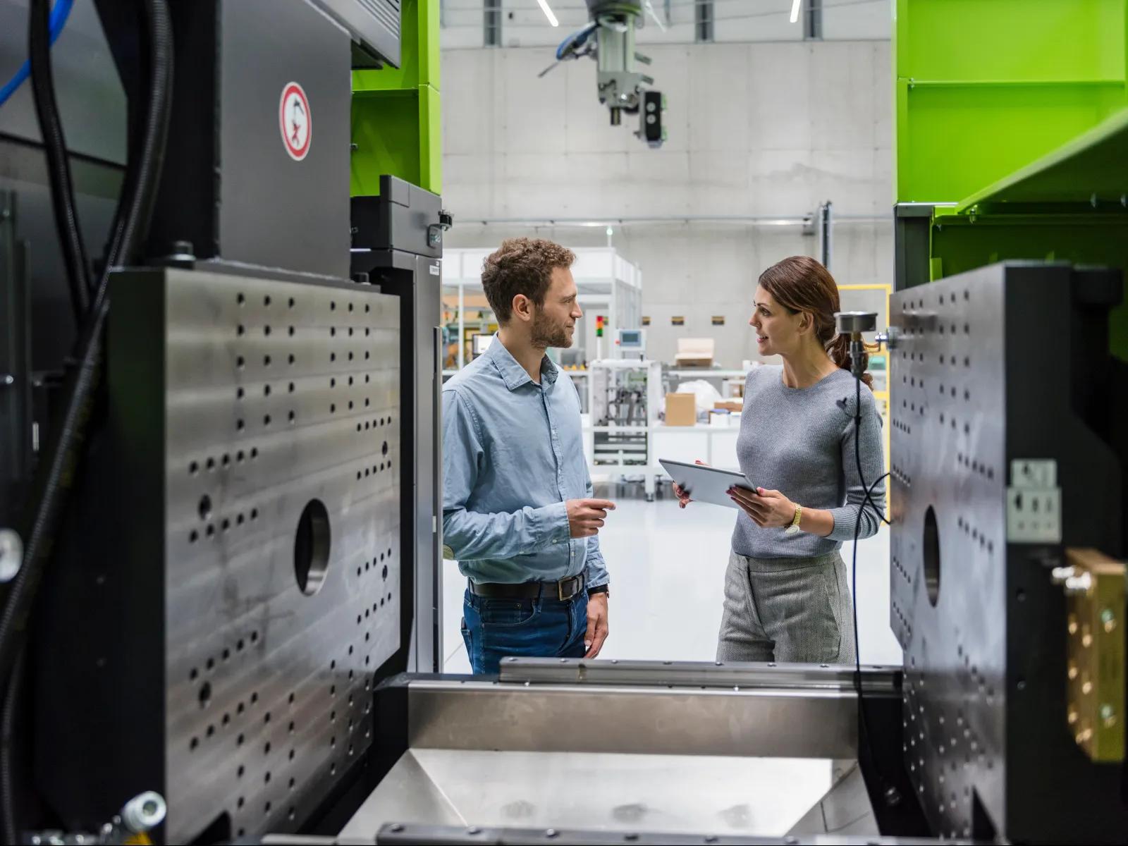 Two engineers discussing work inside a modern industrial manufacturing facility with large machinery.