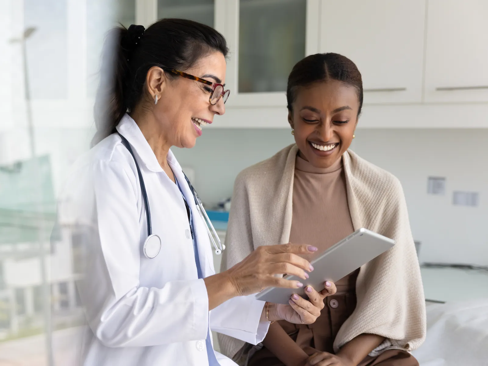 Doctor showing tablet to smiling patient in modern medical office during consultation