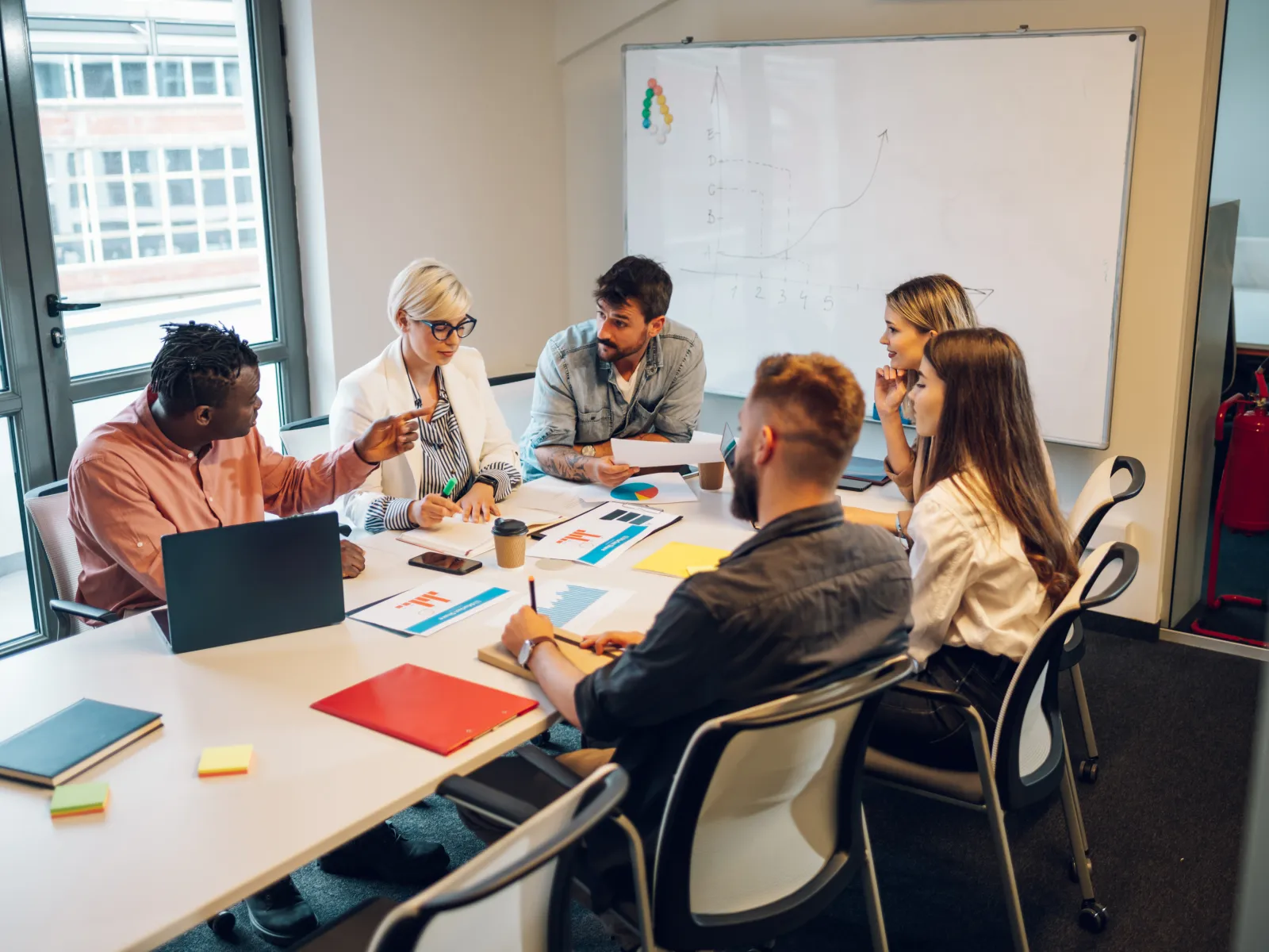 Diverse group of colleagues discussing charts and laptops around a meeting table in a modern office.