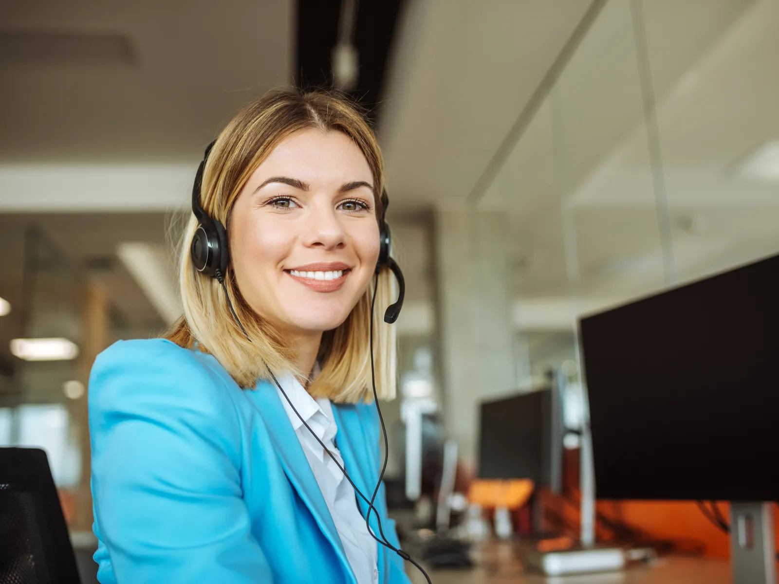 Smiling female customer service representative wearing headset in modern office environment.