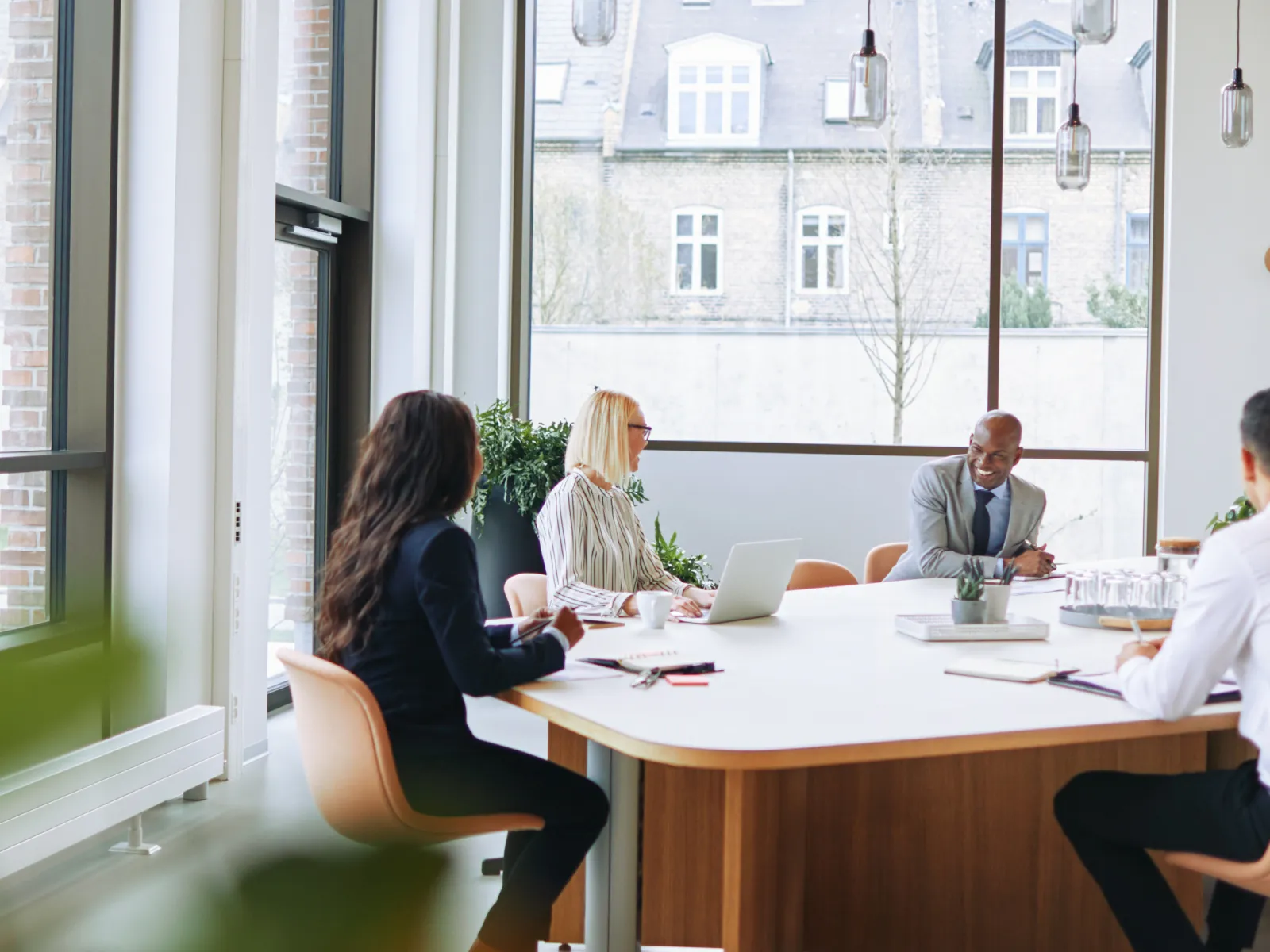 Diverse business team in formal attire having a meeting around a large white table in a bright office.