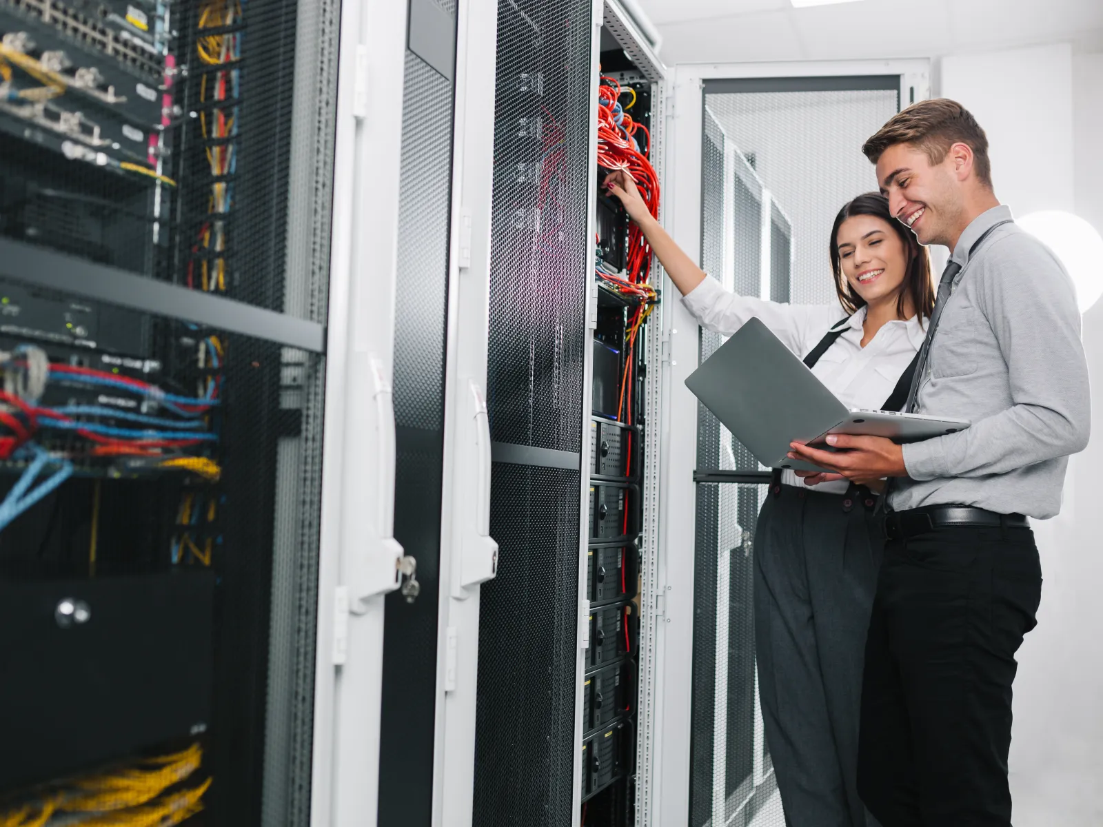 Two IT professionals managing cables and using a laptop inside a modern server room with racks.