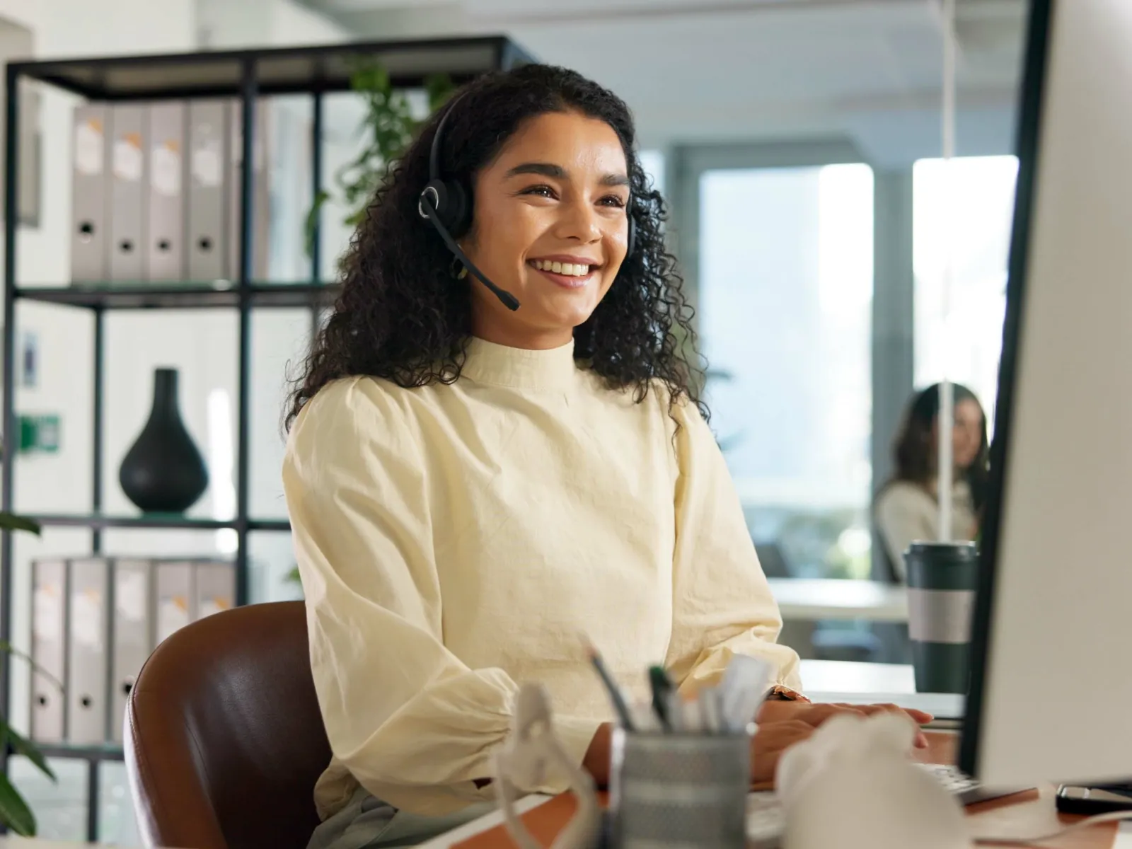 Smiling customer service representative wearing headset working at computer in modern office environment