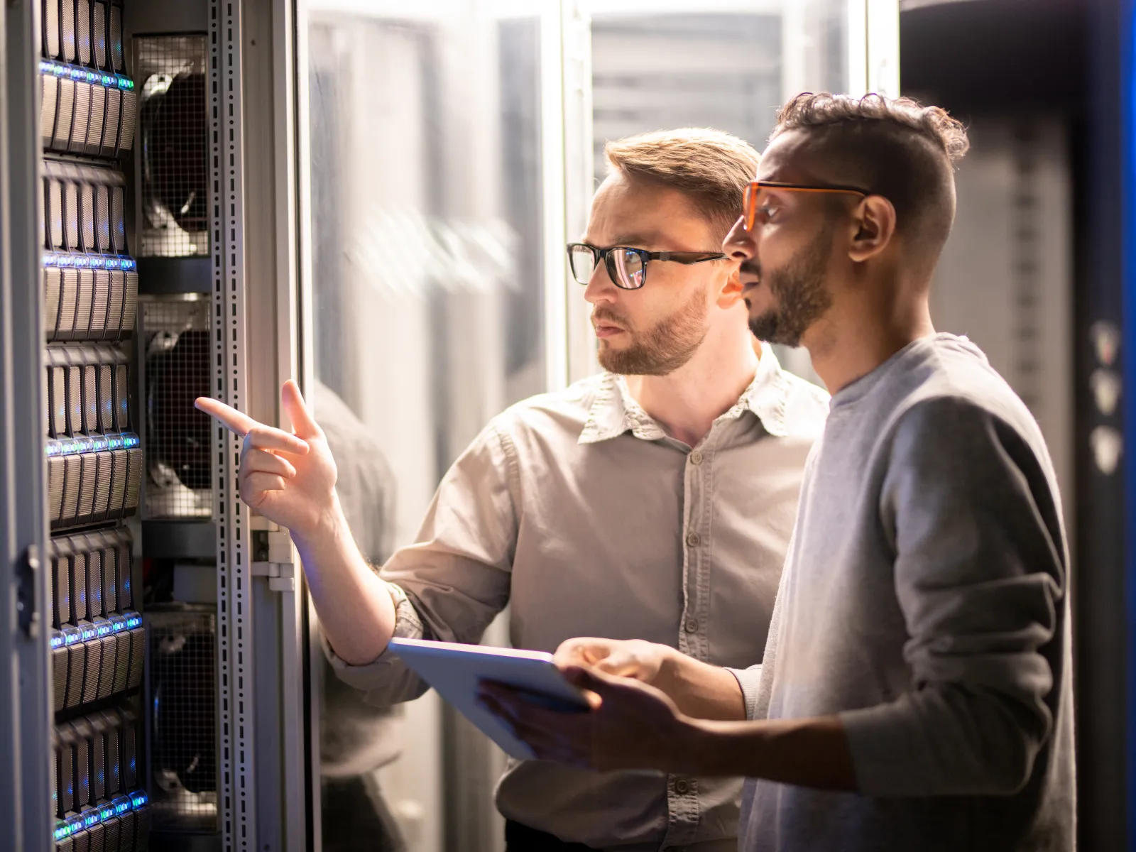 Two IT professionals analyzing server hardware in a data center with tablet and focused expressions