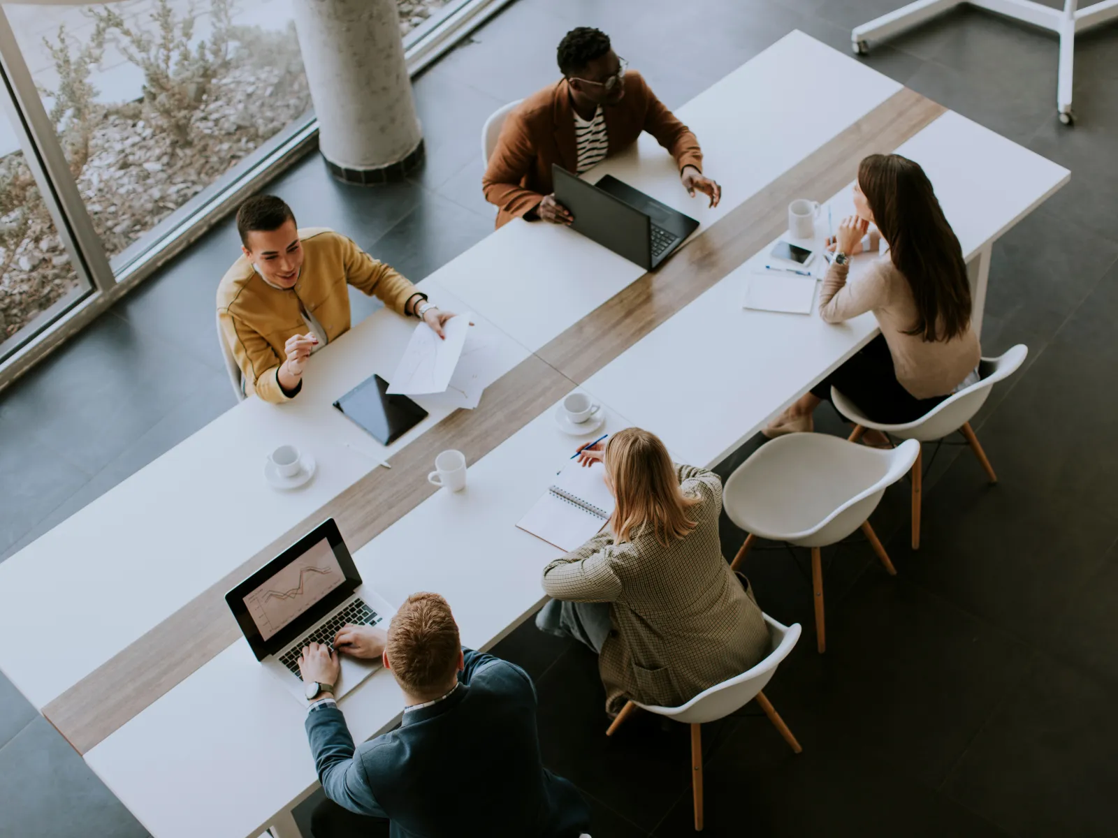 Overhead view of a diverse team having a meeting around a modern office table with laptops and documents.