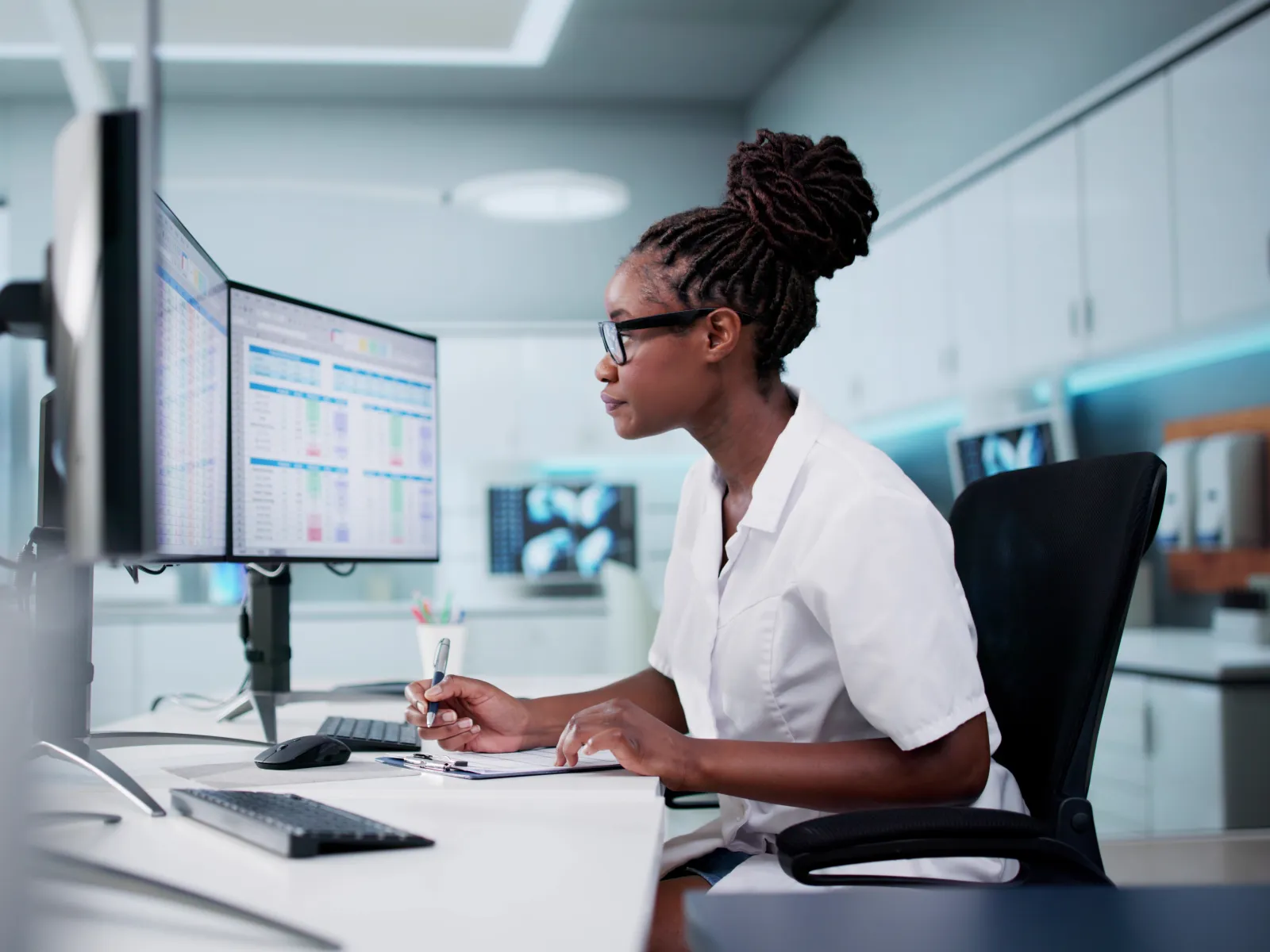 Healthcare professional analyzing data on dual monitors in a modern medical office environment.