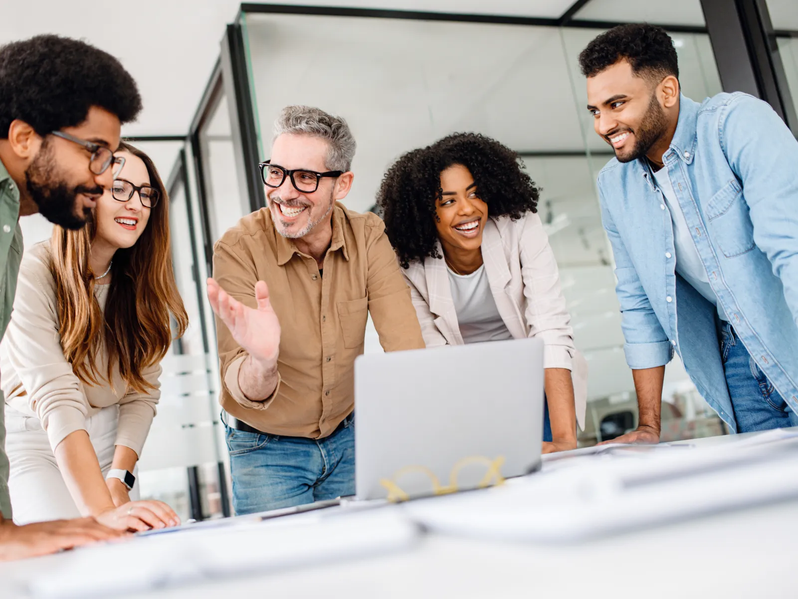 Diverse group of coworkers smiling and discussing ideas around a laptop in a bright modern office.