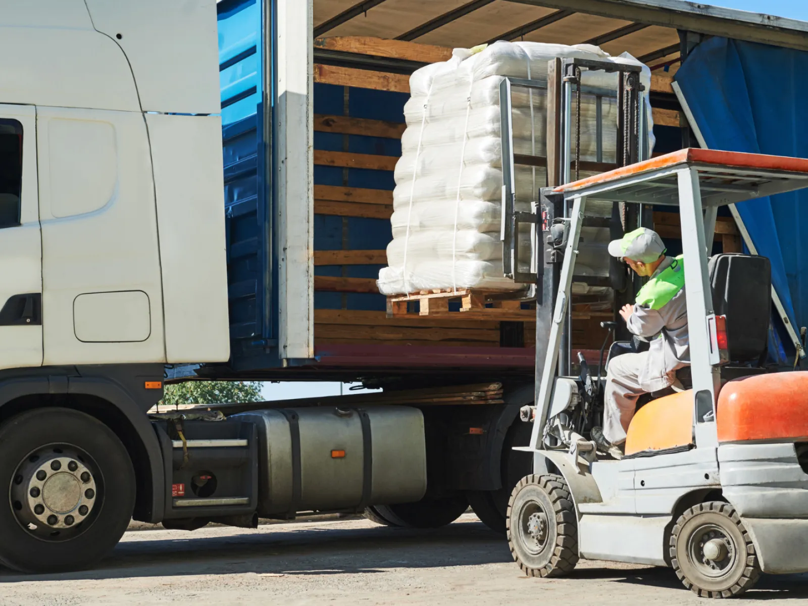 Worker operating forklift to load pallet of goods into a white cargo truck at a warehouse loading dock.