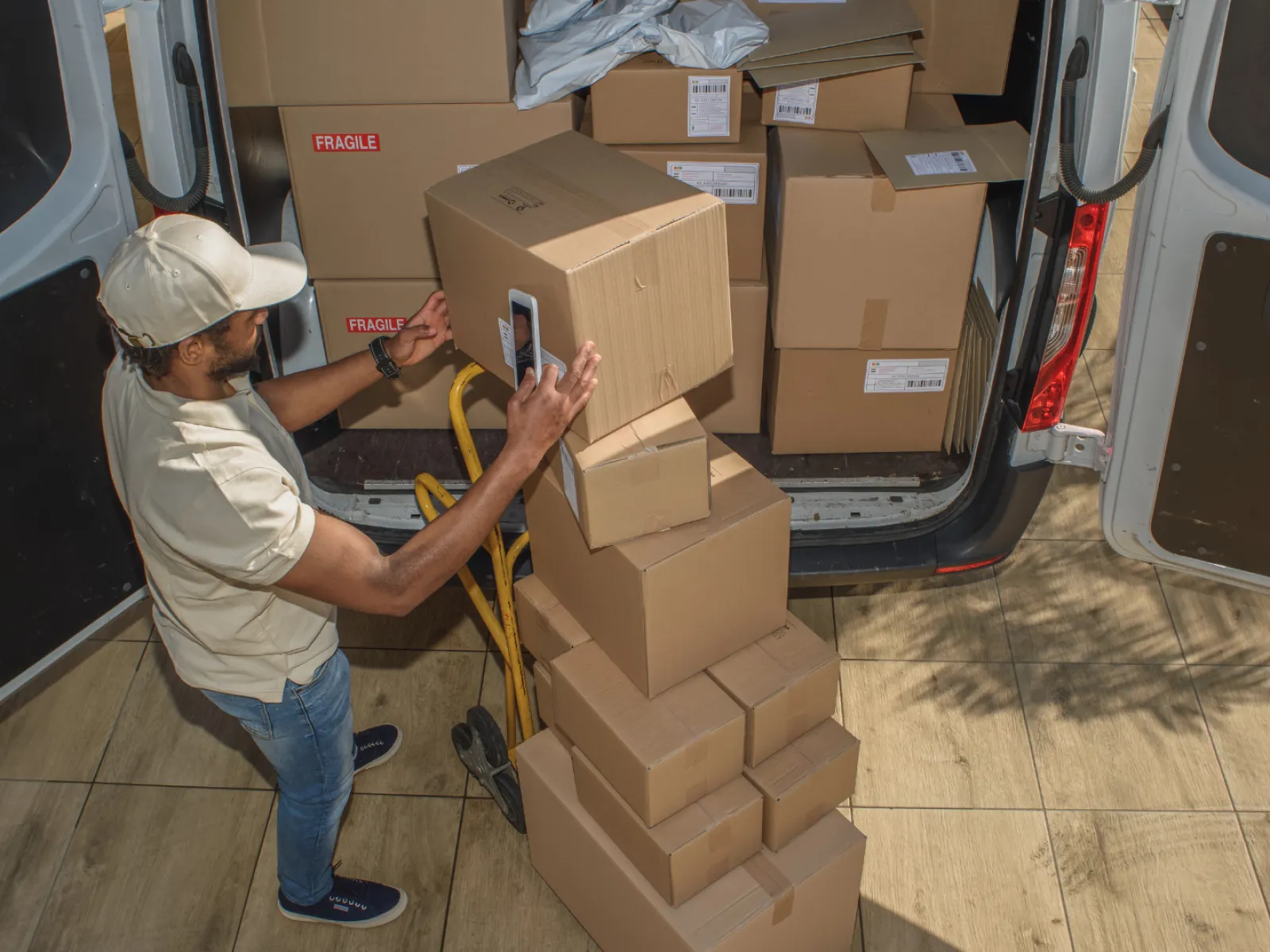 Delivery worker scanning barcode on stacked cardboard boxes outside a delivery van for shipment.