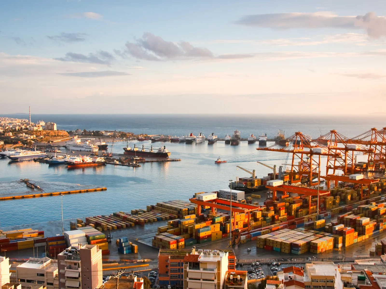 Aerial view of a bustling container port with cranes, ships, and colorful cargo containers under a partly cloudy sky.