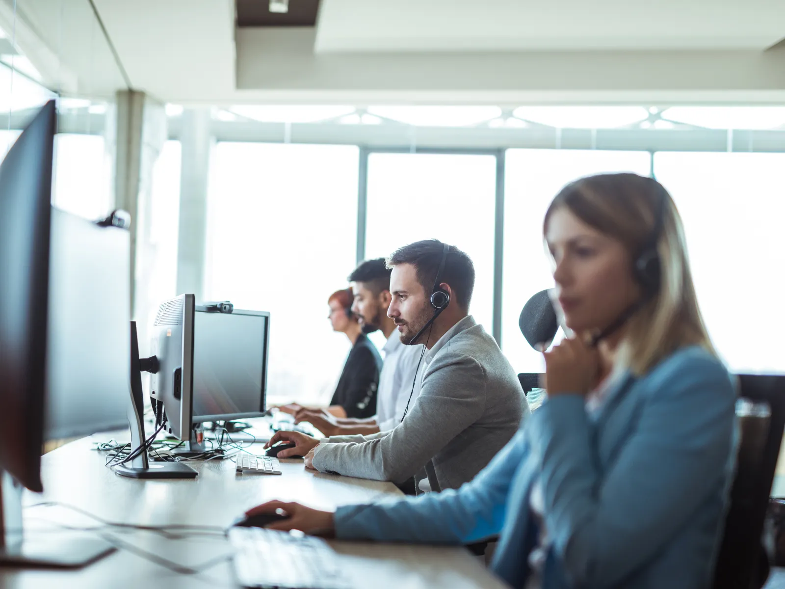 Call center employees with headsets working on computers in a bright modern office environment.