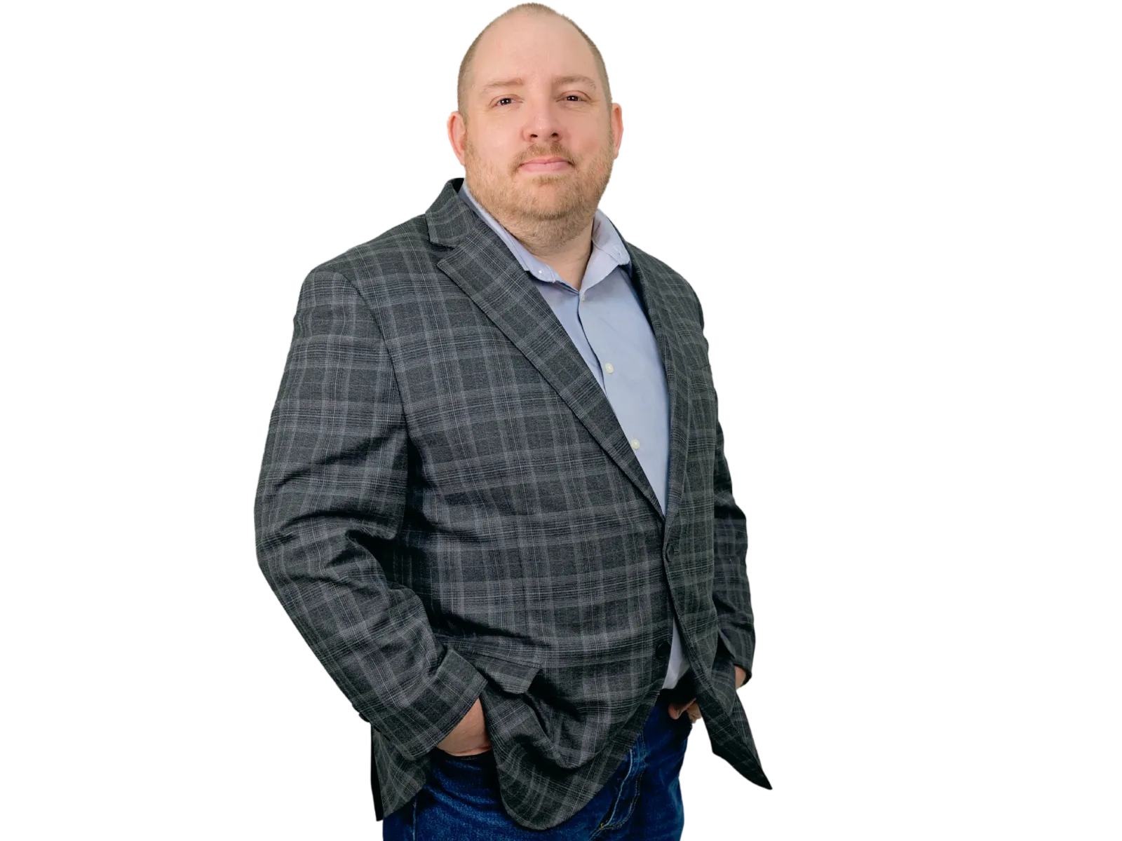 A man in a plaid blazer and jeans stands confidently against a black background.