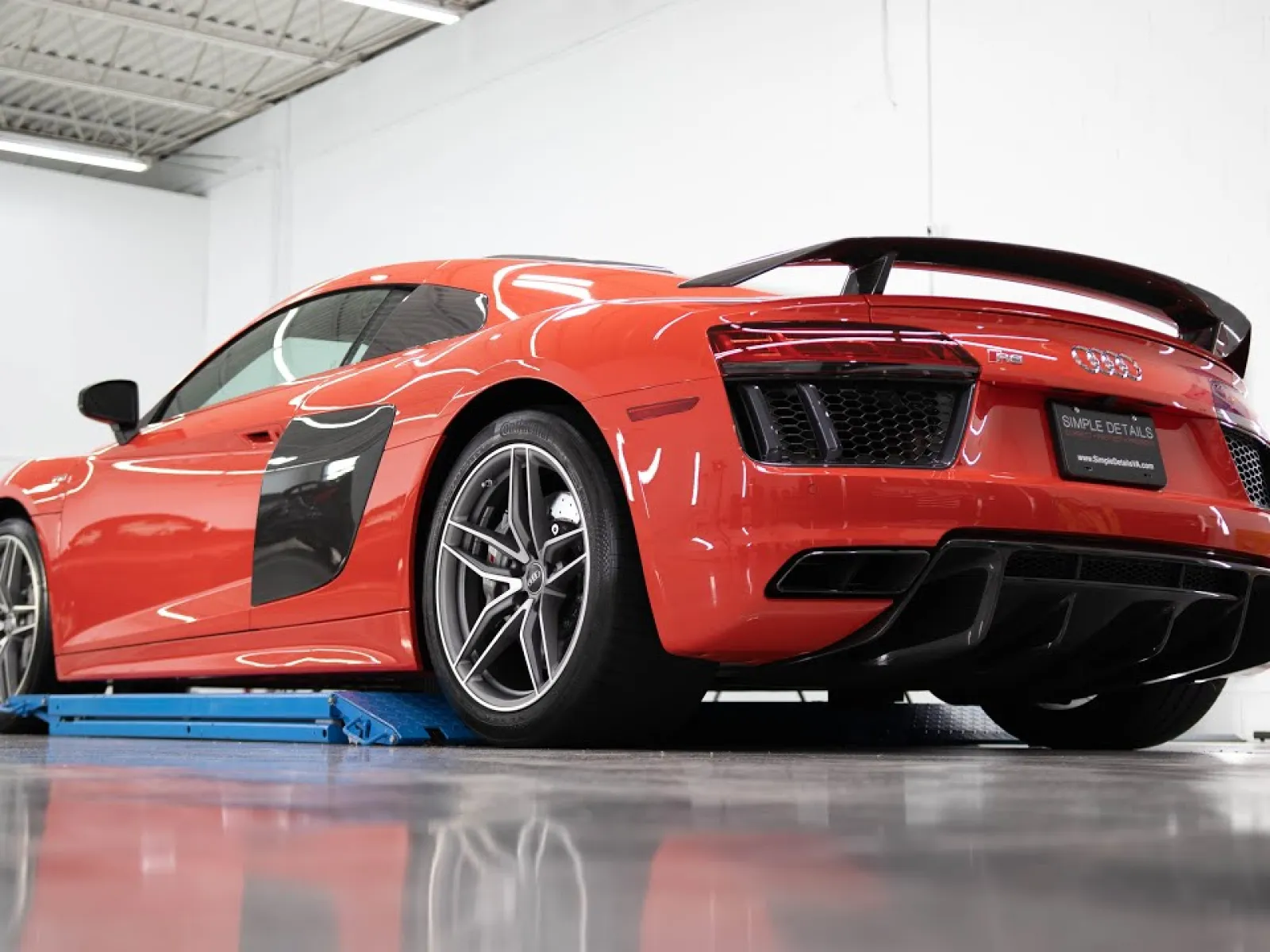 Red Audi R8 sports car seen from rear side inside a garage on a glossy floor.