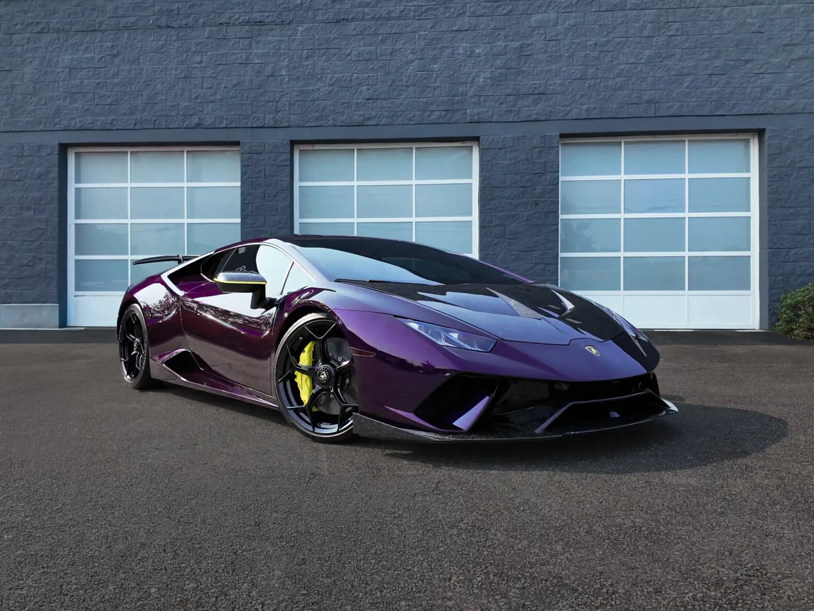 Glossy purple Lamborghini sports car parked in front of modern garage doors on asphalt.