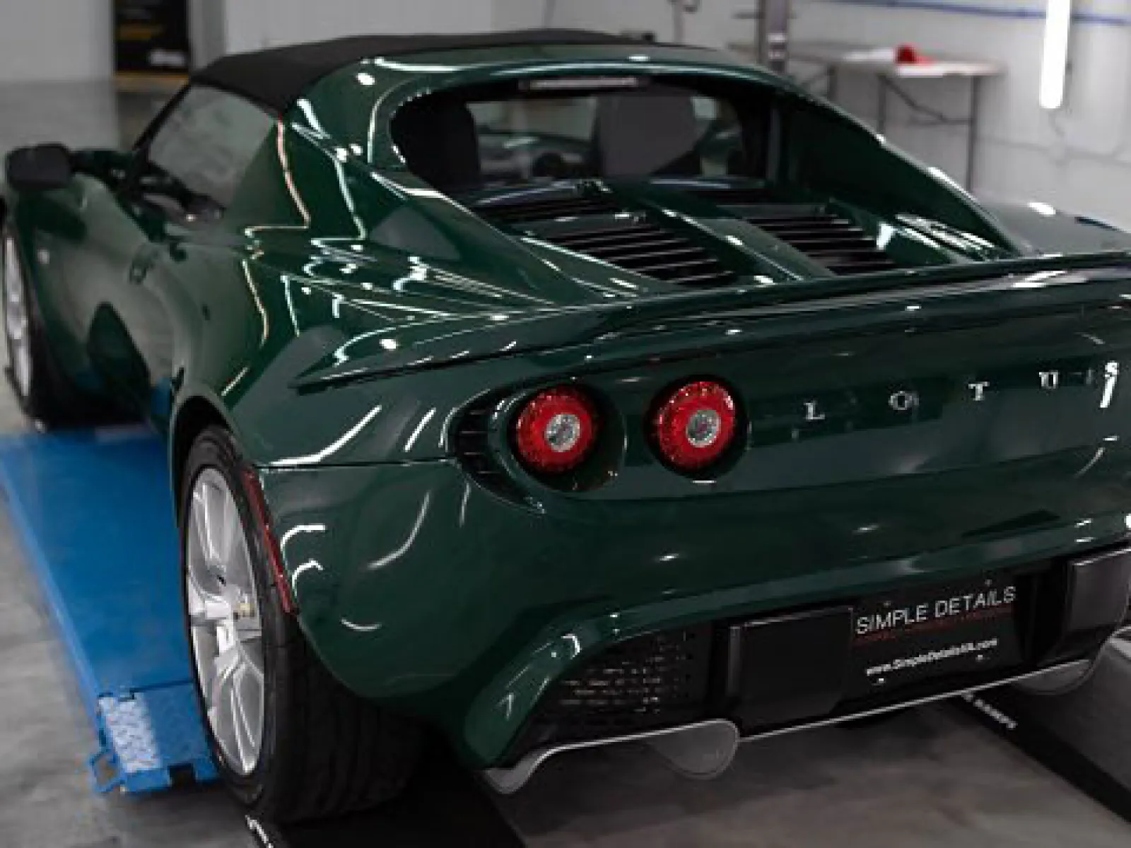 Rear view of a dark green Lotus sports car with round taillights in a garage setting.
