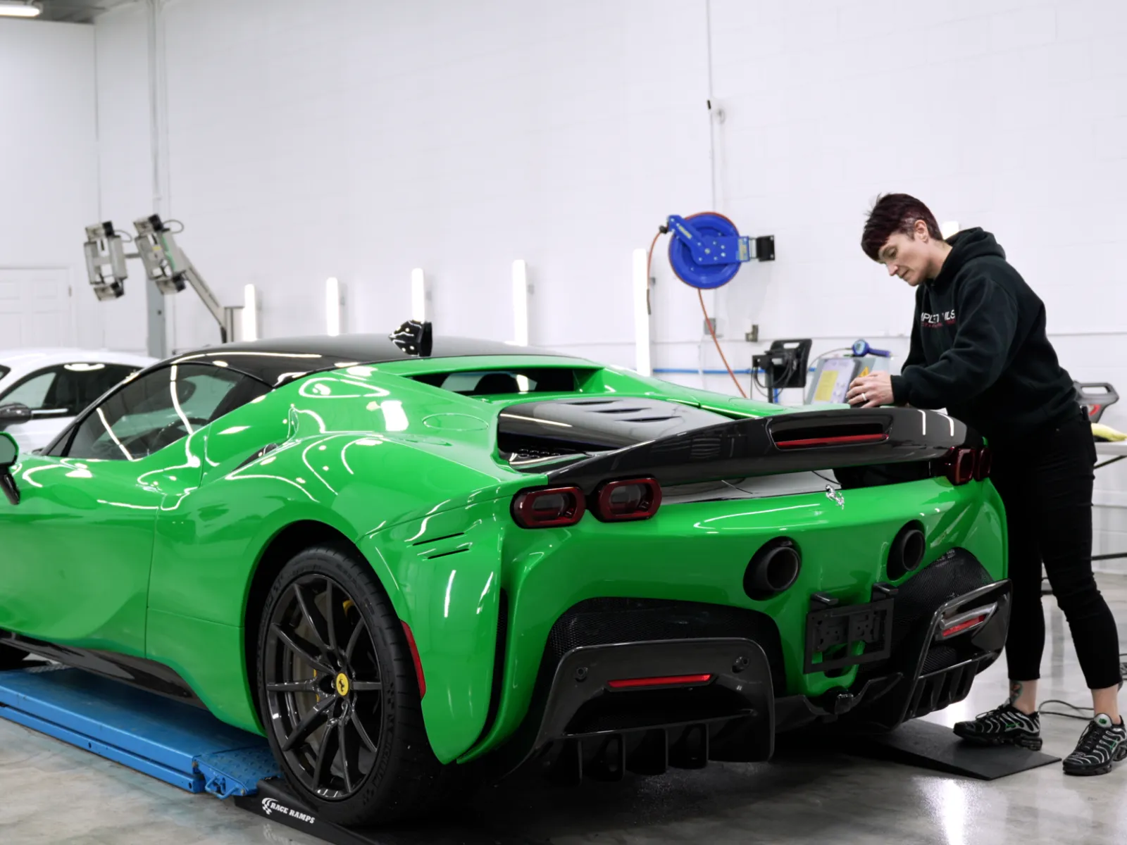 Green Ferrari sports car and white Porsche GT4 in a garage with a person detailing the Ferrari.