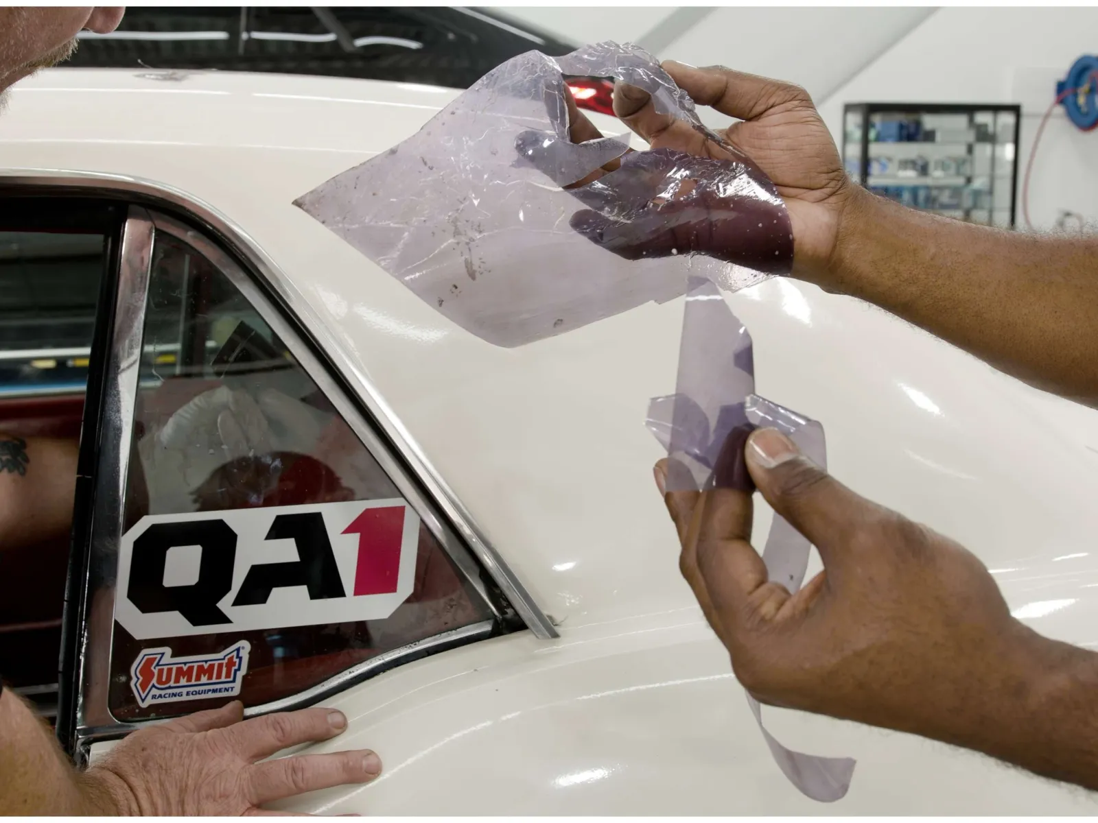 Person applying protective film to white car's side window near QA1 and Summit Racing stickers.