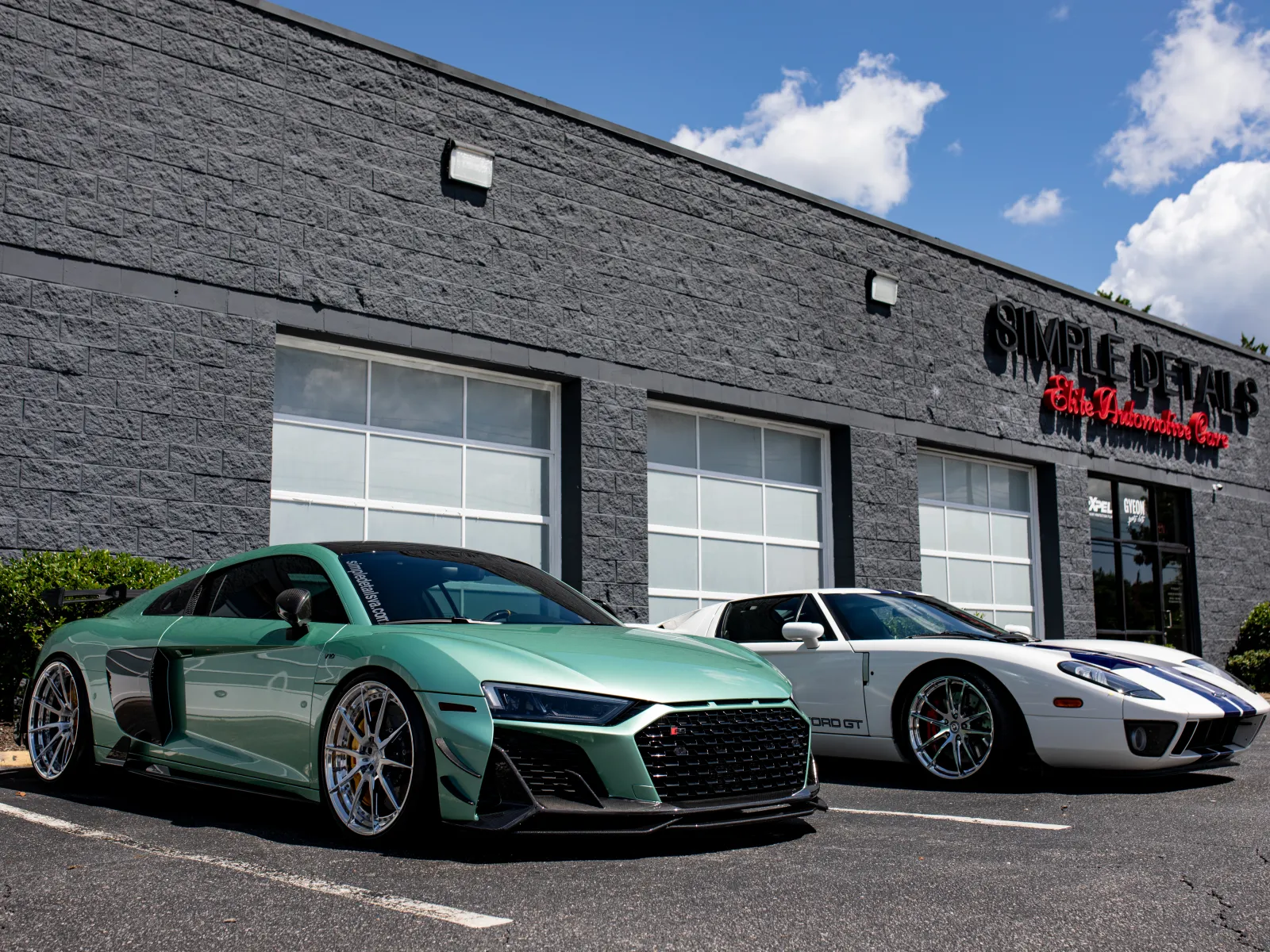Green Audi R8 and white Ford GT sports cars parked outside Simple Details car detailing shop on a sunny day