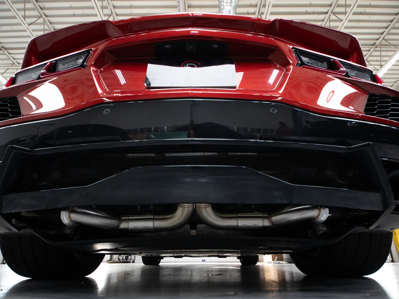 Low angle view of the rear red sports car showing exhaust pipes and aerodynamic rear diffuser in a garage.