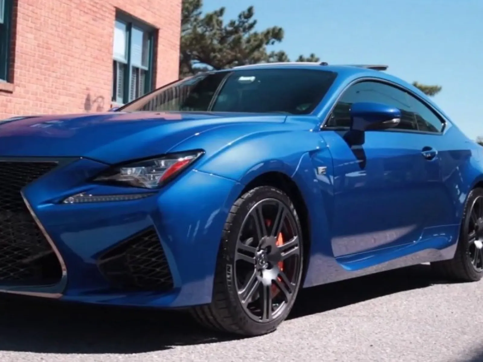 Blue Lexus sports car parked on a street near a brick building under clear sky.