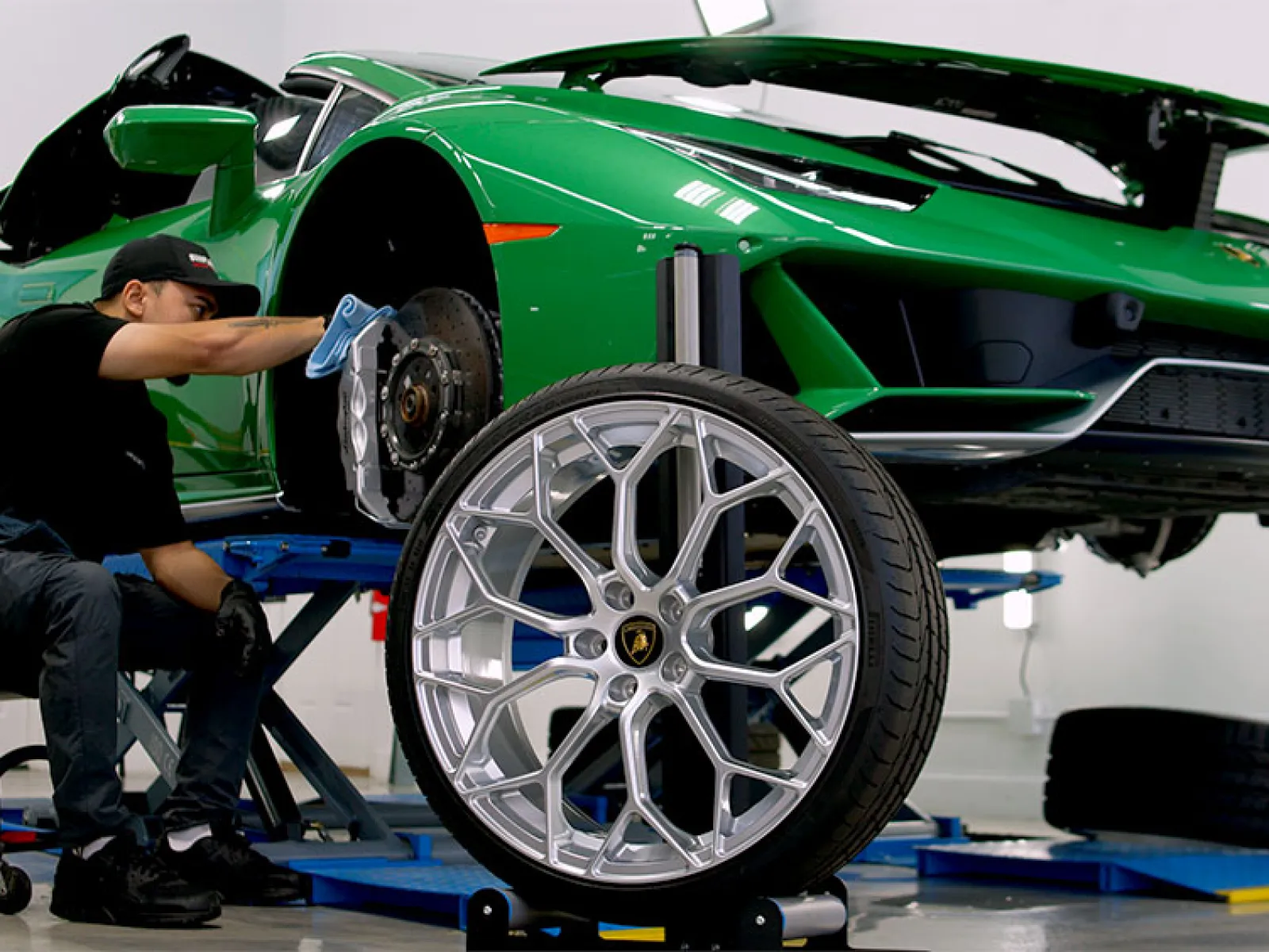Mechanic installing a silver alloy wheel on a green sports car lifted in a bright auto repair shop