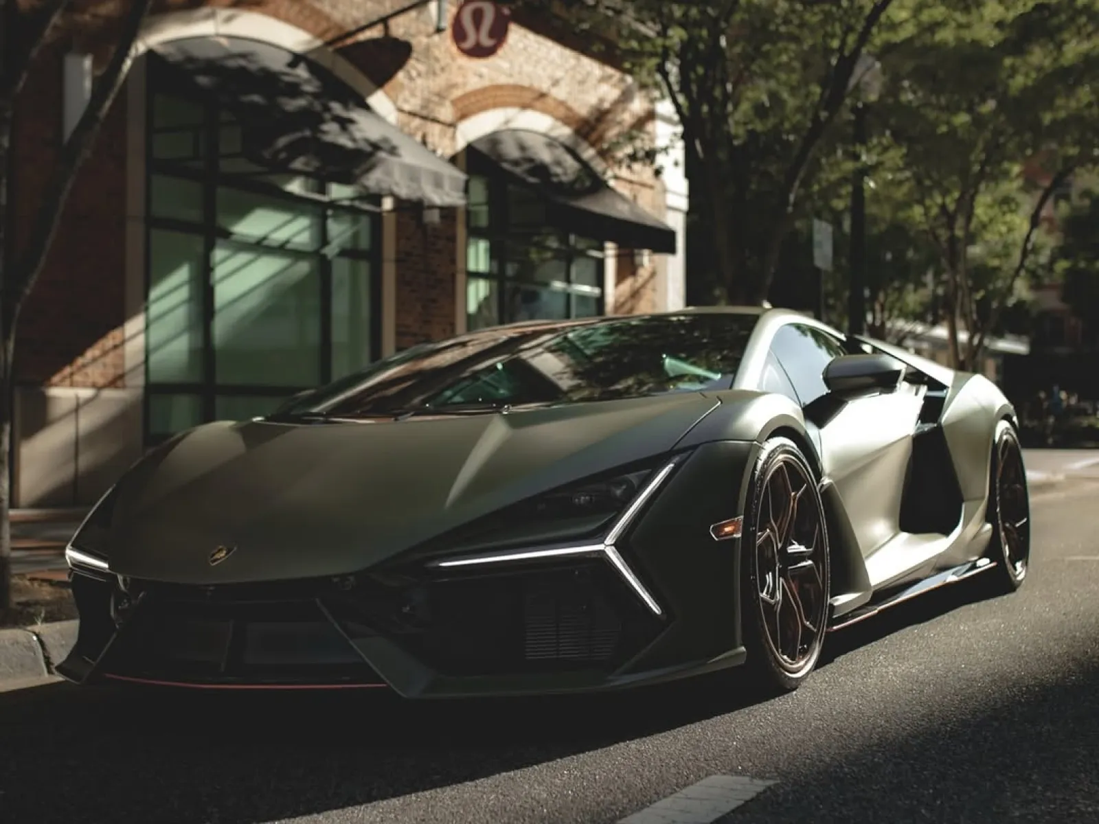 Matte black Lamborghini Sián sports car parked on a sunlit city street near a brick building.