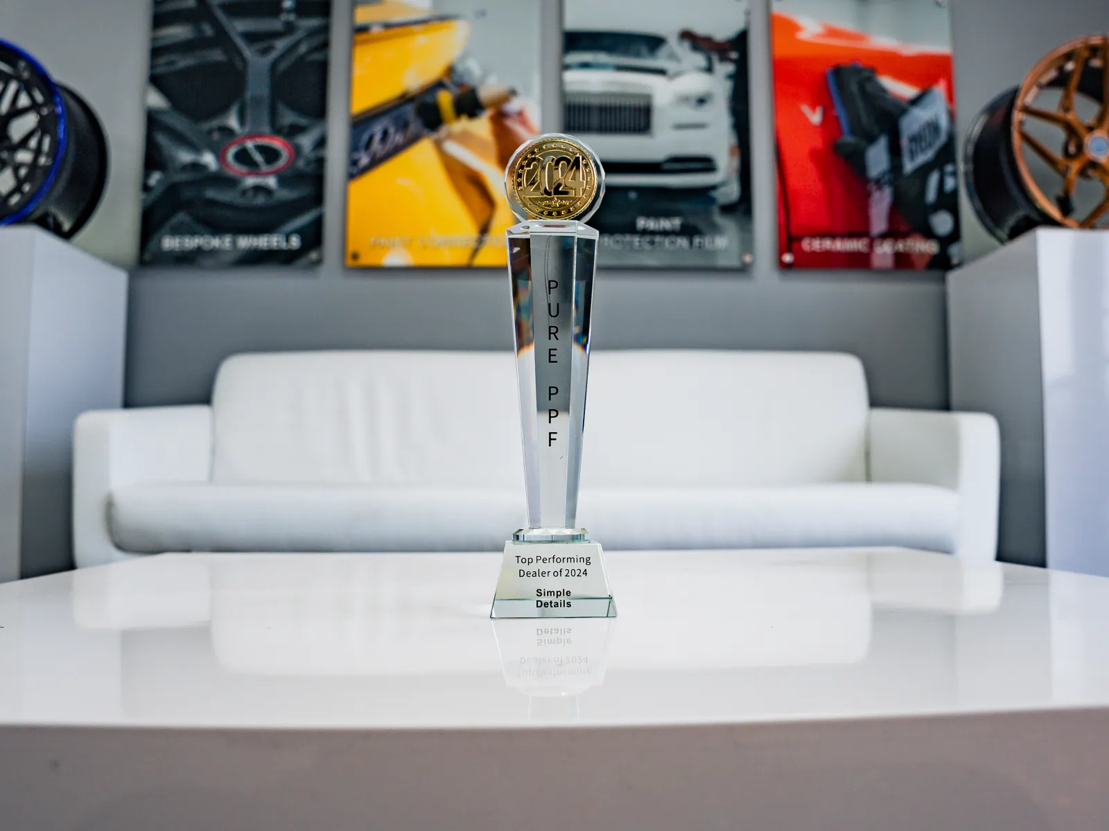 Trophy labeled Pure PPF for Top Performing Dealer 2024 displayed on white table with couch and car wheels in background