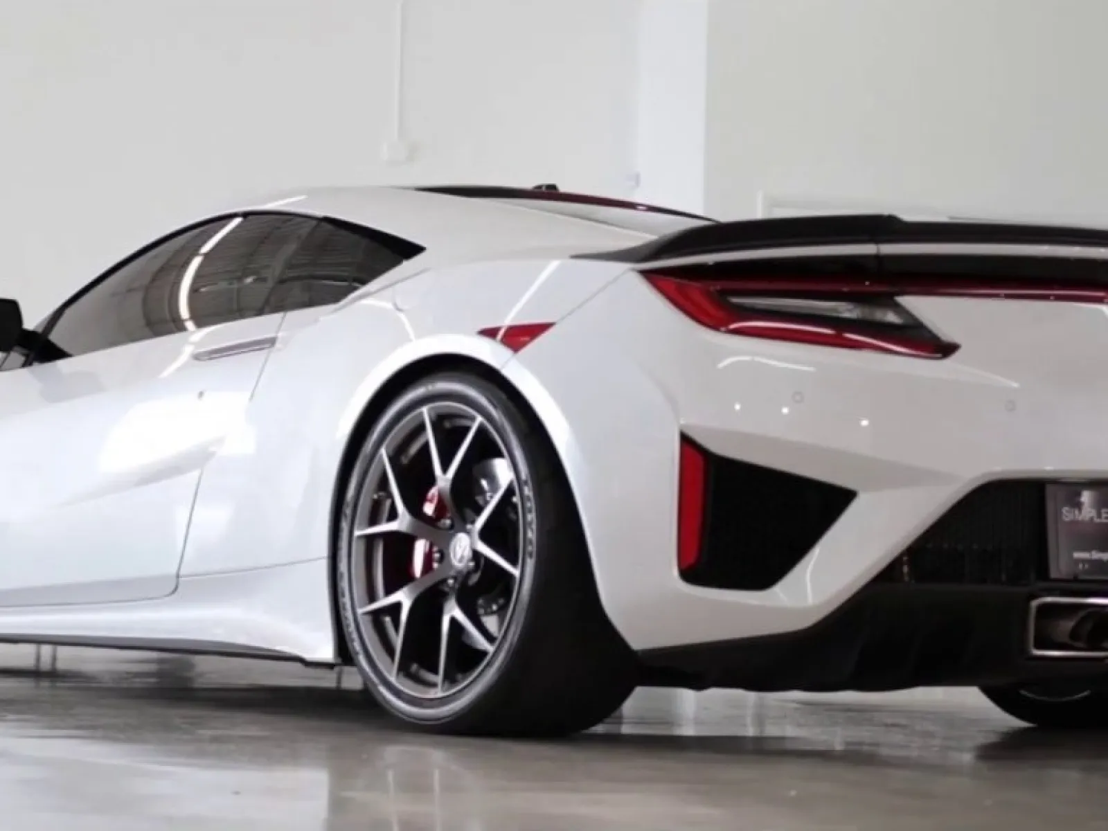 Sleek white sports car with black rims parked inside a bright garage with polished concrete floor.