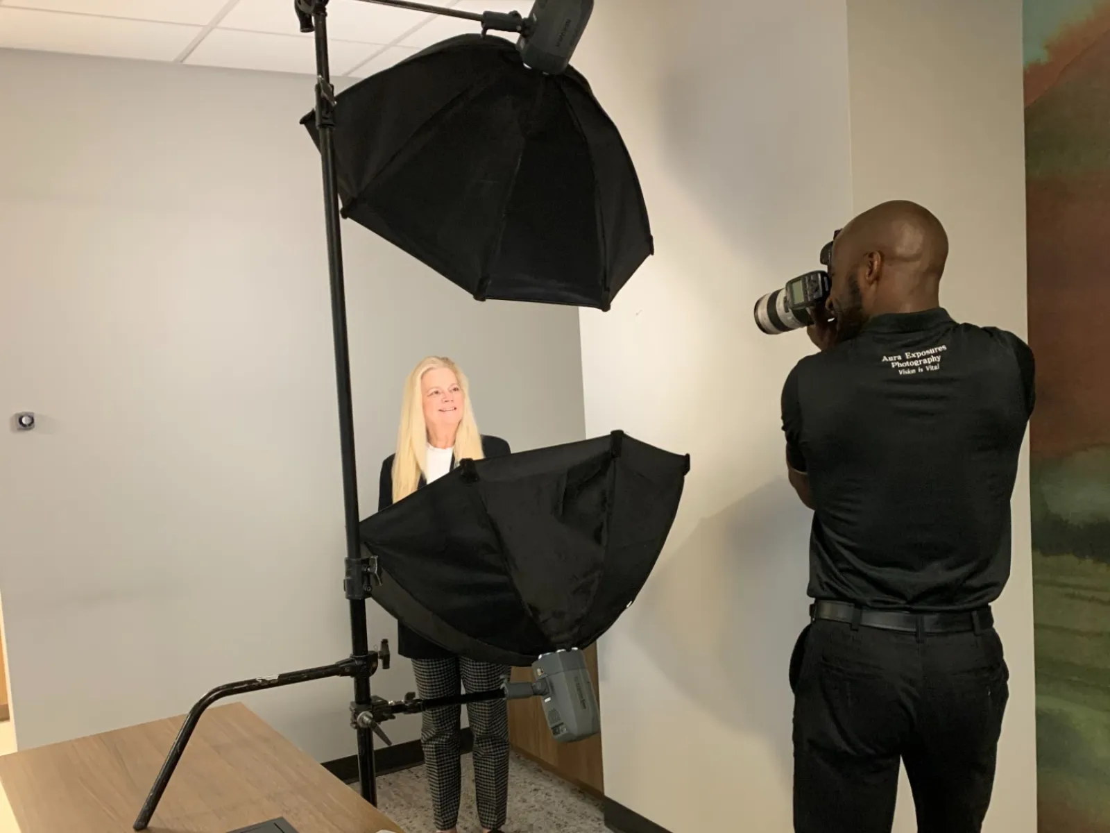 Photographer takes studio portrait of a woman with professional lighting and camera setup indoors.