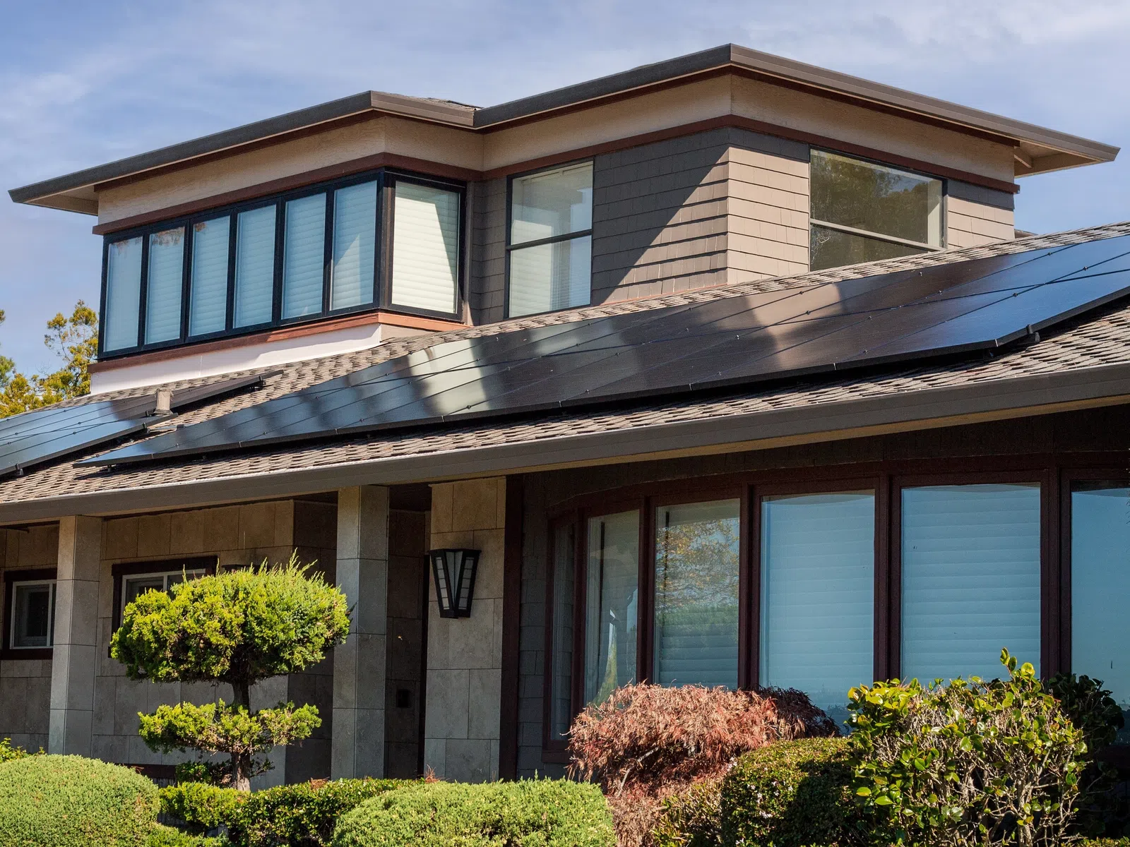 Modern house with solar panels on the roof surrounded by green shrubs and trees under a clear sky.