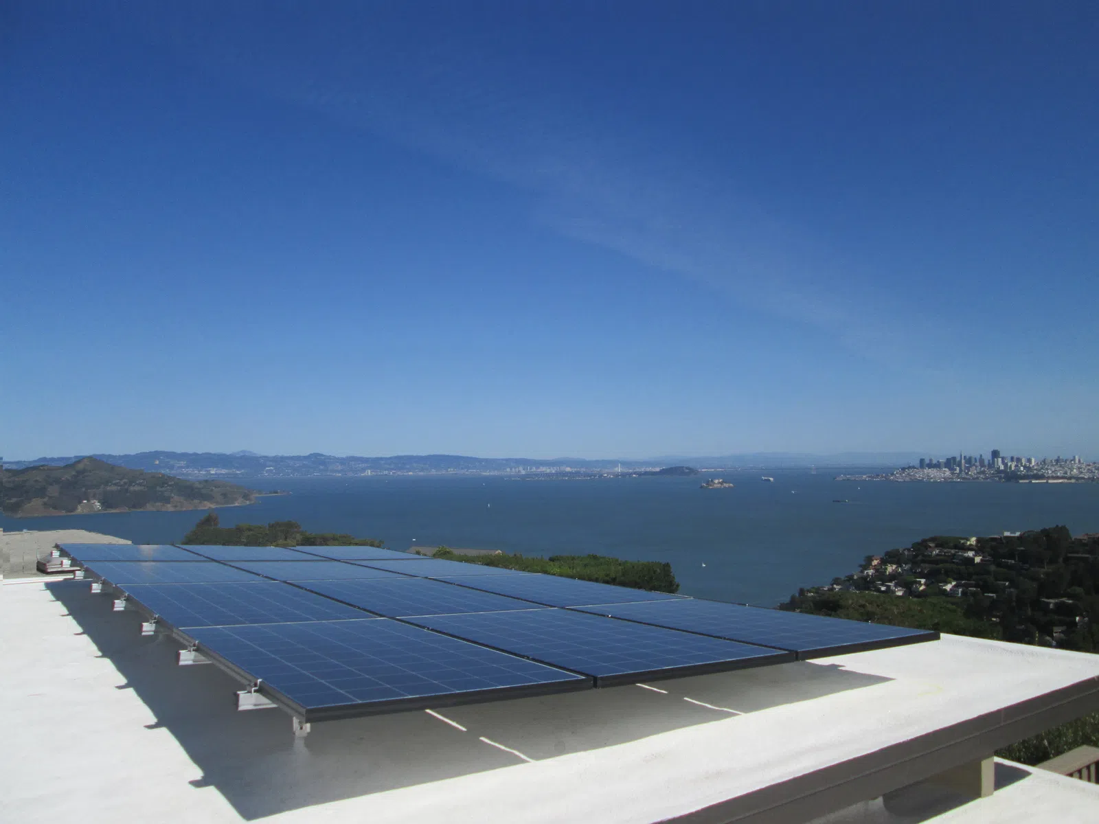 Solar panels installed on a rooftop overlooking a bay with a city skyline in the background under a clear blue sky.