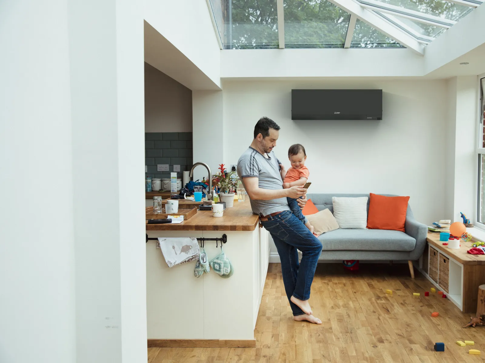 Father holding baby while checking phone in bright living room with electric HVAC heat pump air conditioning